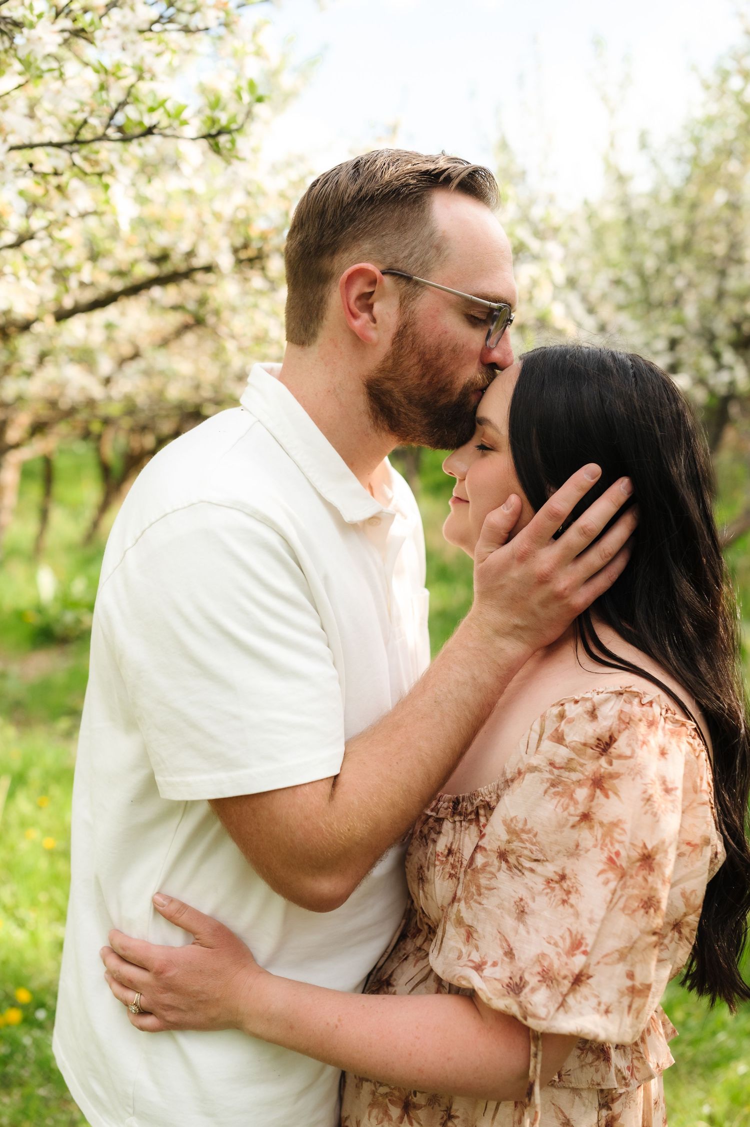 Intimate couple shares tender moments in a beautiful spring orchard setting with white flowering trees.