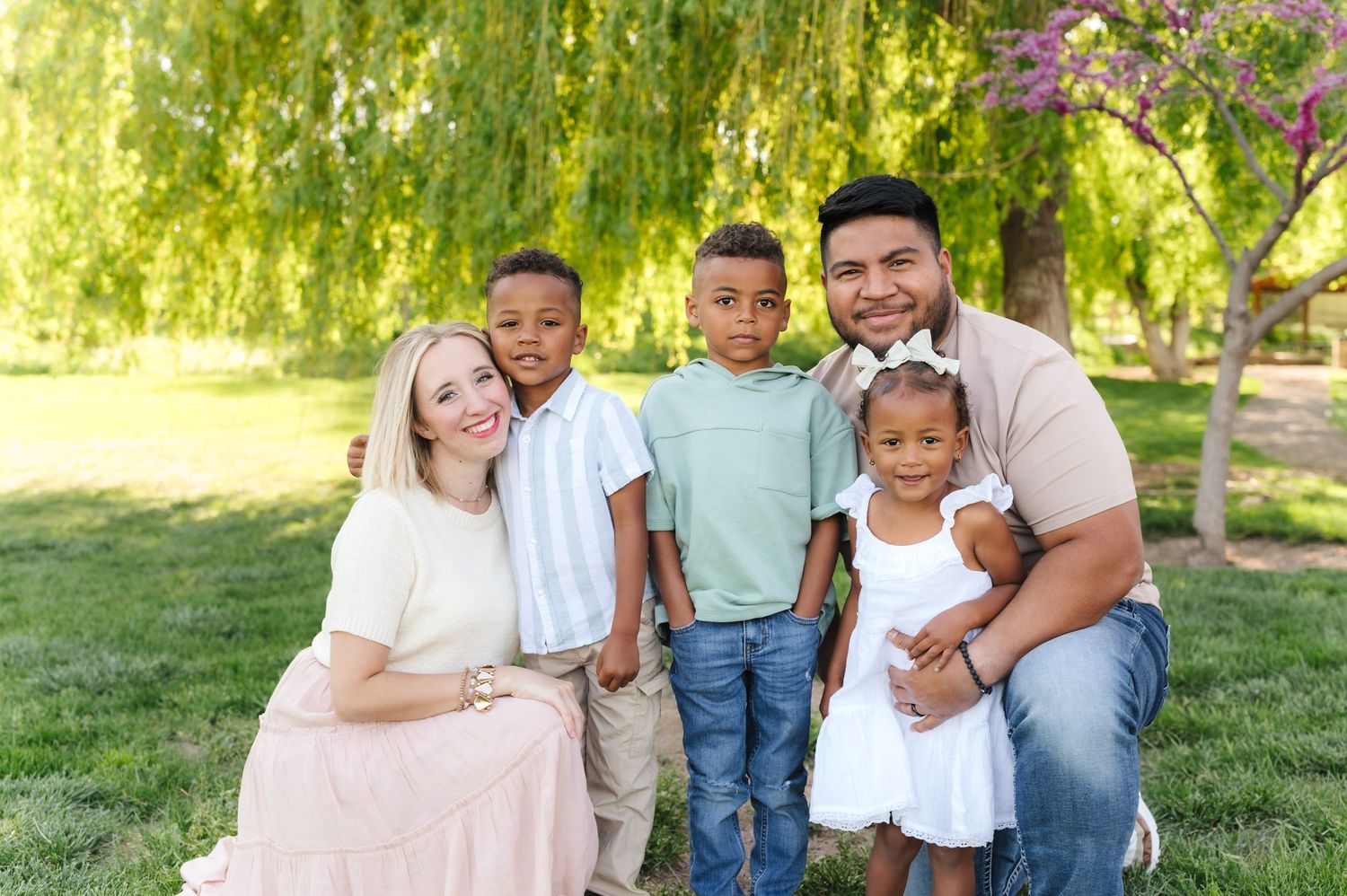 A group shares joyful moments together under weeping willow trees in a sunny park setting.