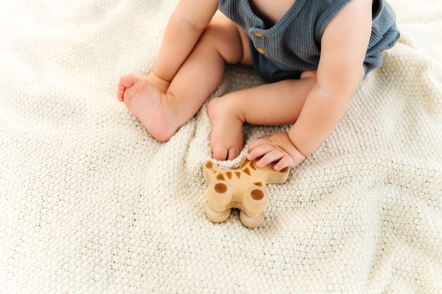 Close-up of baby feet and hands playing with wooden toys on white blanket.