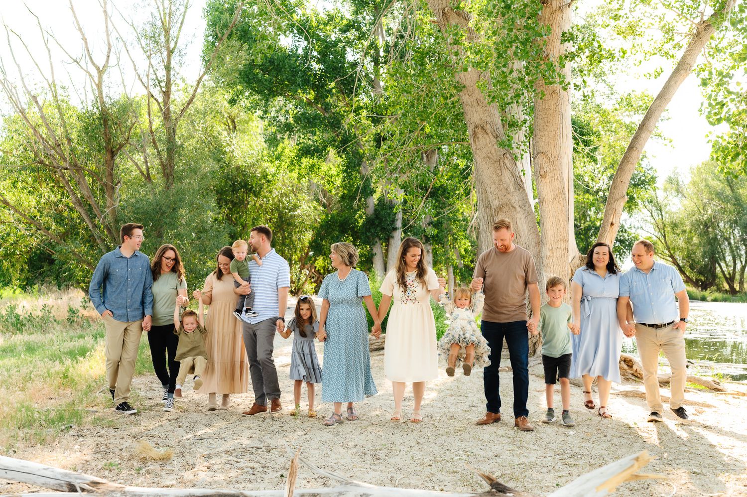 Family gathering photo shoot in a natural setting with trees and dappled sunlight.