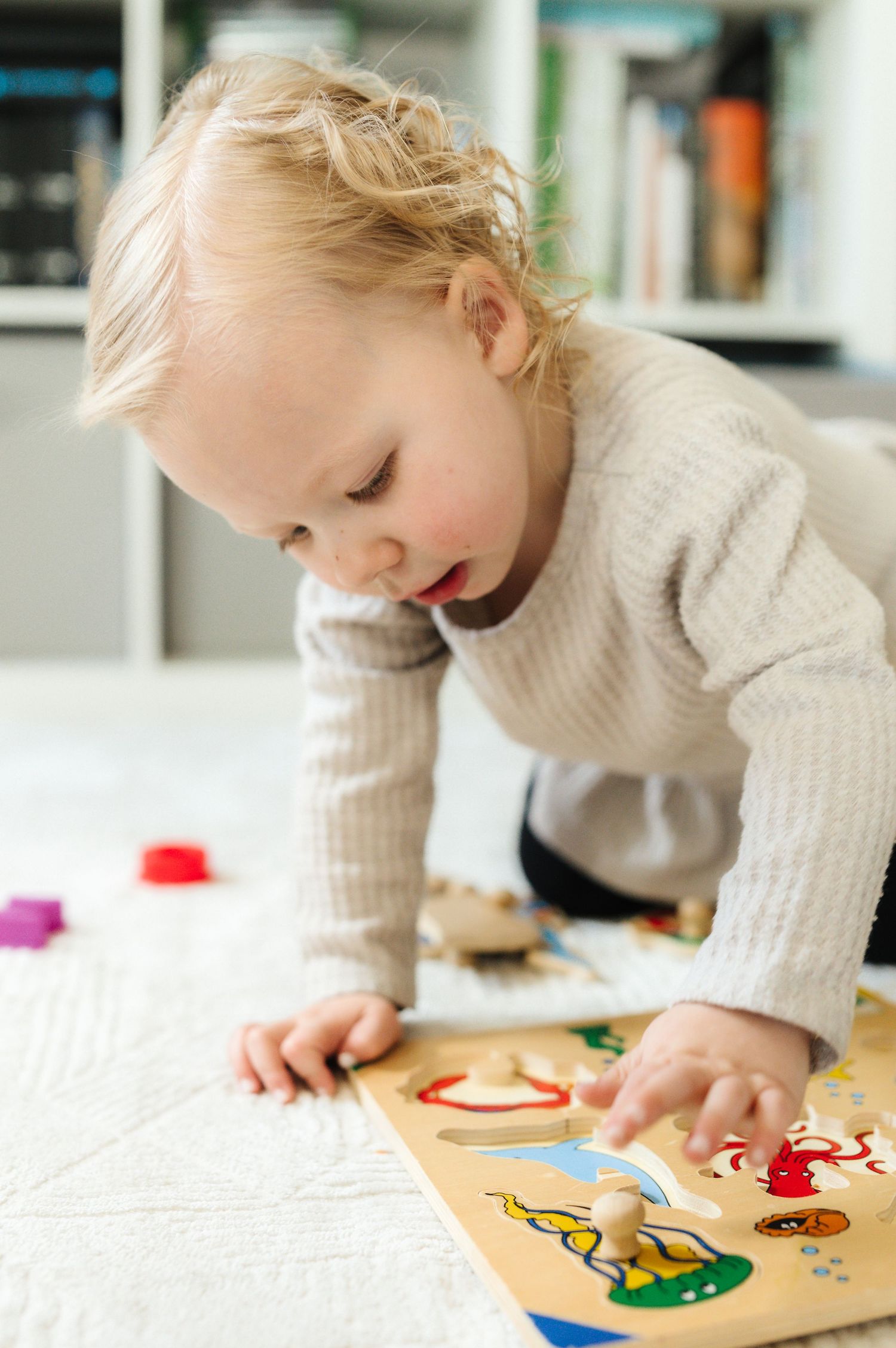 Child playing with wooden peg puzzle featuring colorful shapes and pieces.