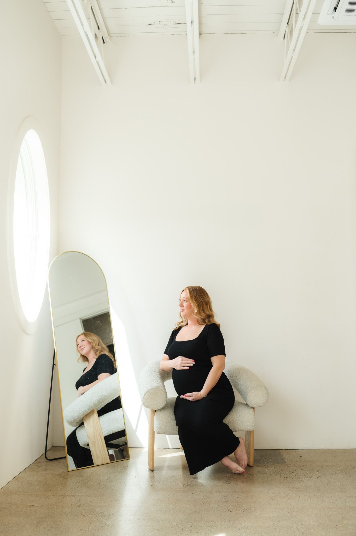 A minimalist studio portrait featuring a black dress against white walls with a mirror reflection.