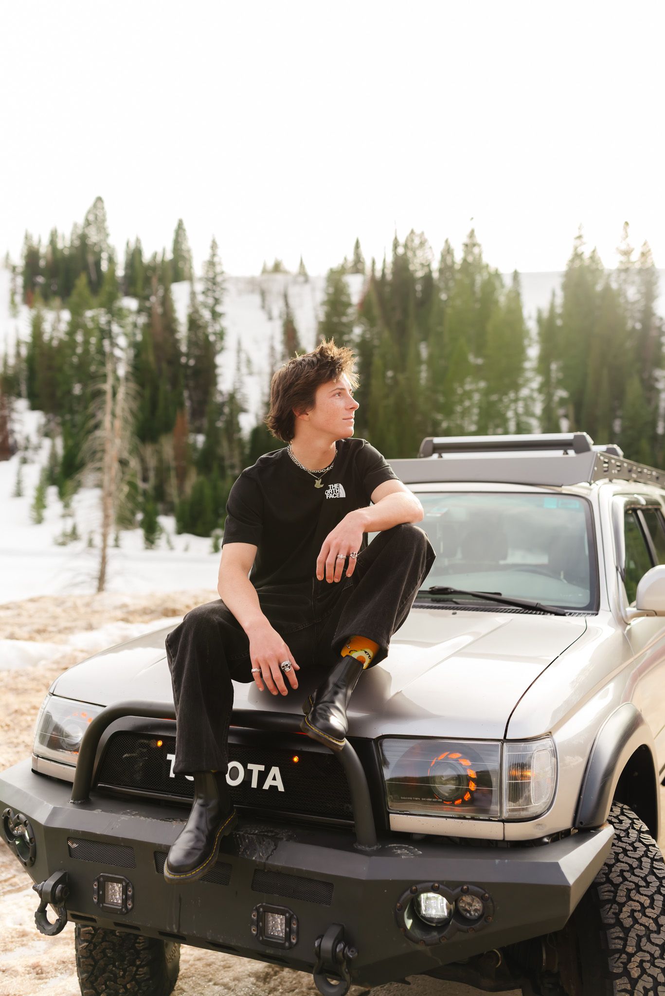 Person sitting on vintage Toyota truck in snowy mountain setting.