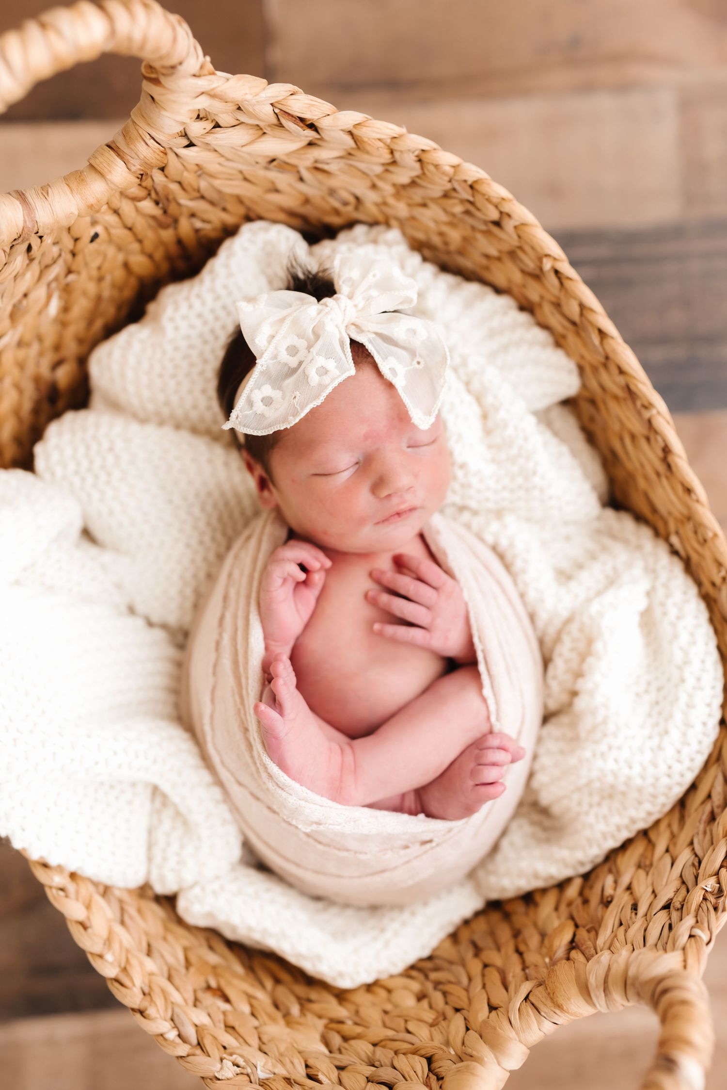 Sleeping newborn wrapped in white blanket nestled in woven basket with floral headband.