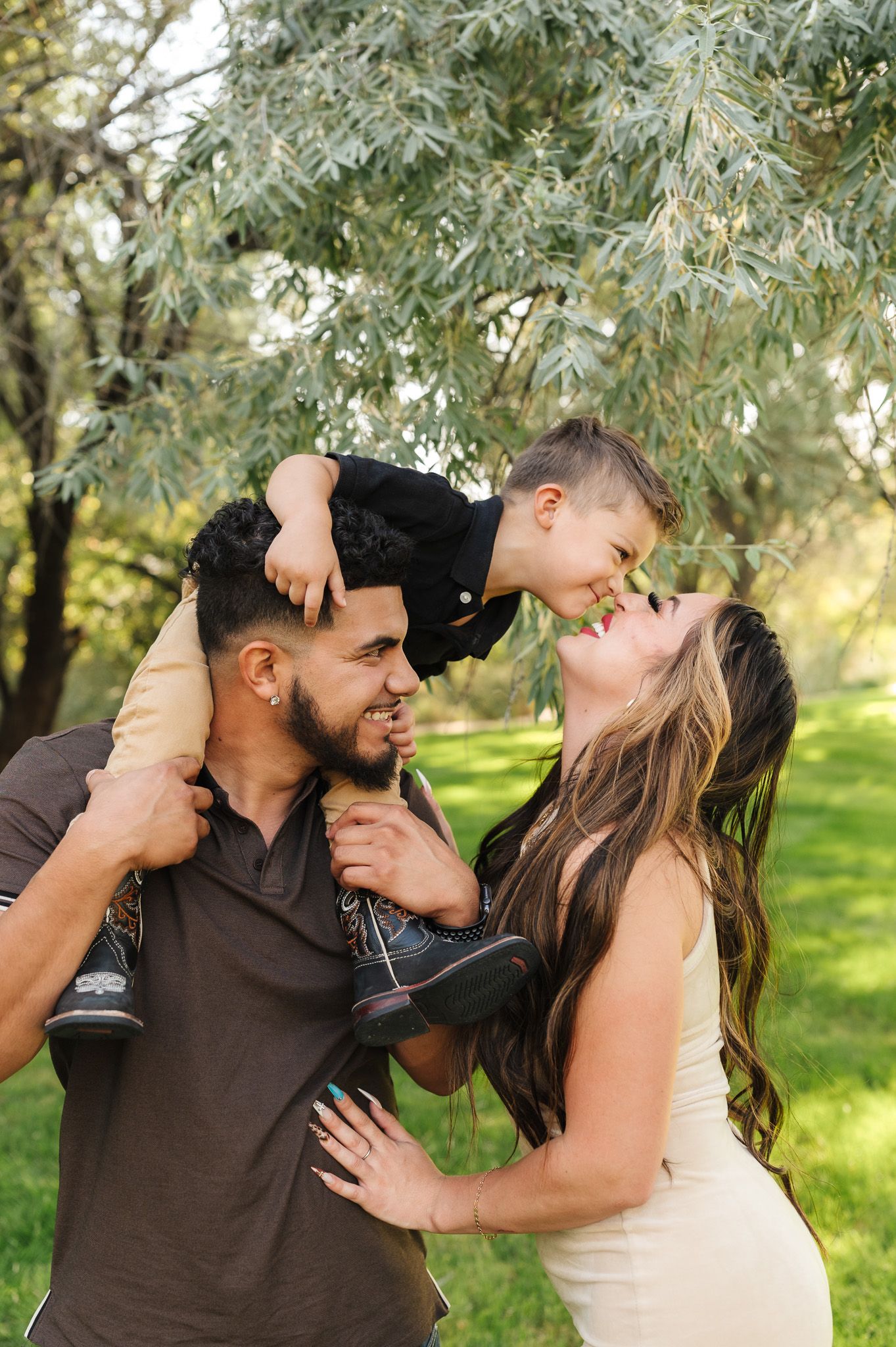 A happy young family with a toddler boy on dad's shoulders, sharing a joyful moment outdoors in a lush green park.
