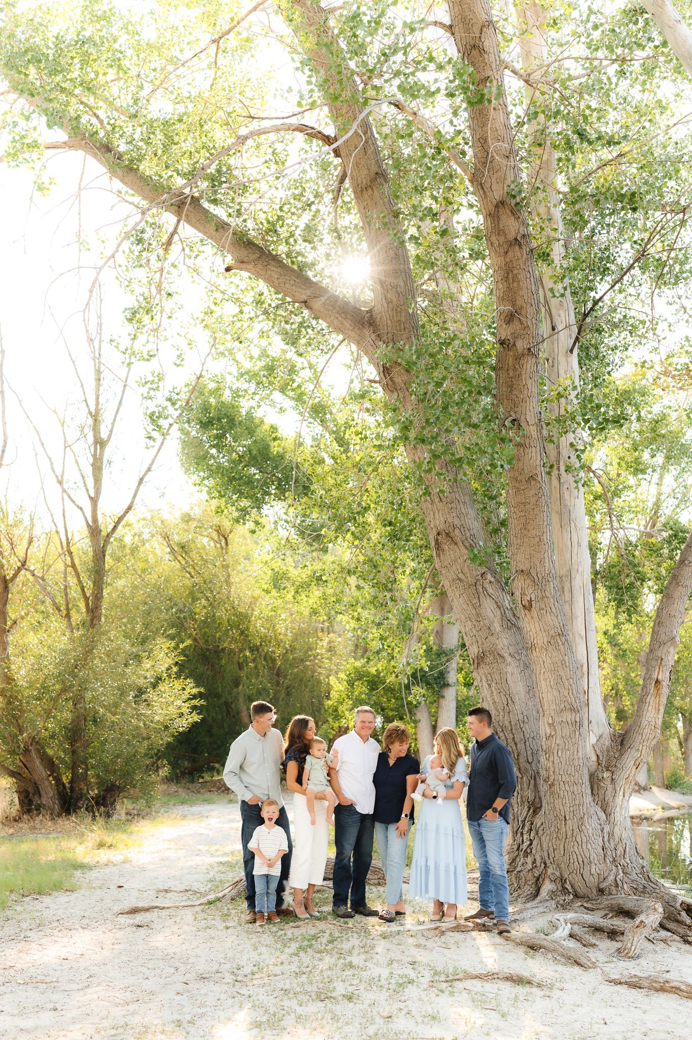 Extended family gathering poses for portraits under large trees in a rustic outdoor setting.