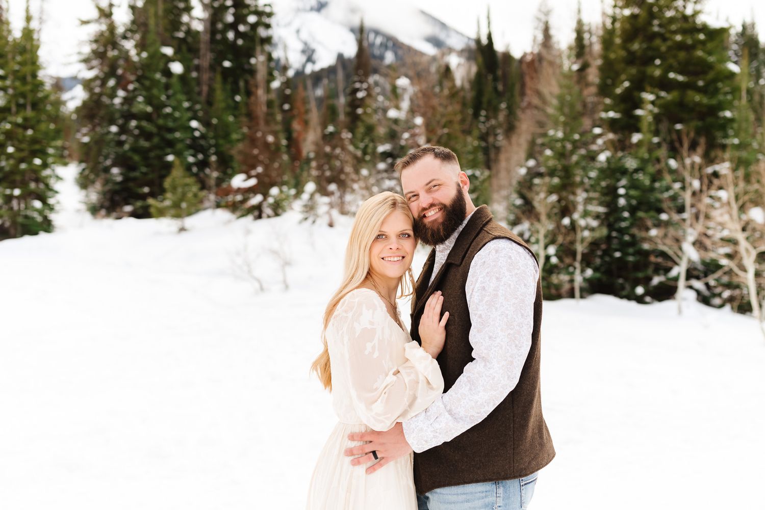 Couple sharing tender moments in a snow-covered mountain forest setting.