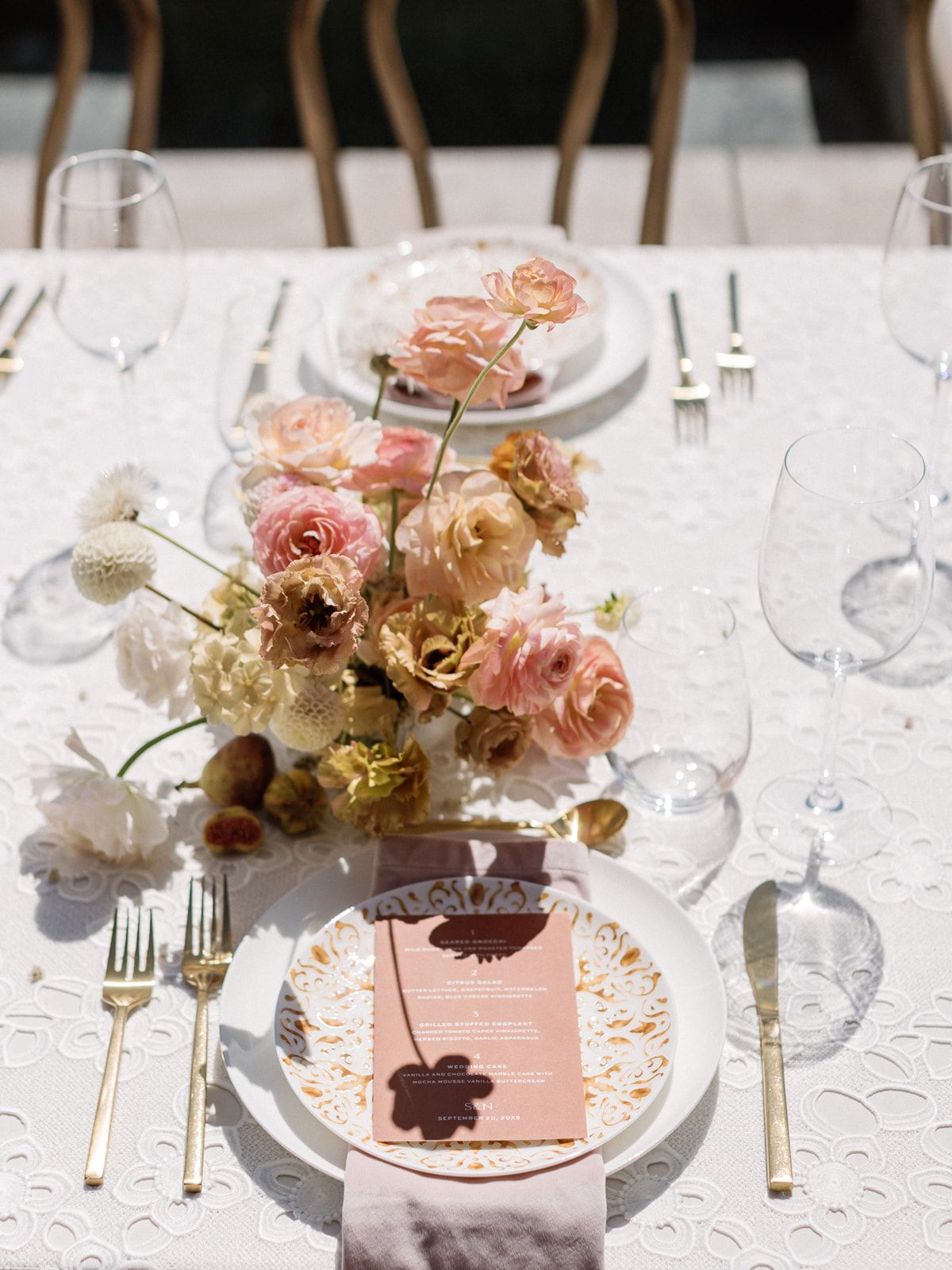 Elegant table setting with pink and gold floral centerpieces, crystal glasses, and delicate place settings on white linens.