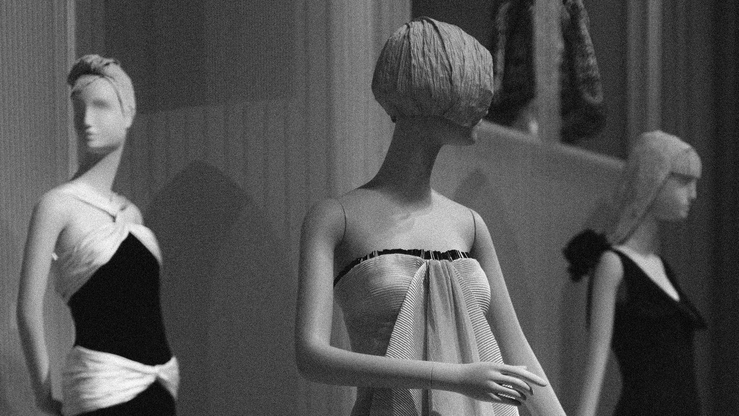 Black and white photo of elegant mannequins displaying vintage fashion gowns in a sophisticated retail store display.