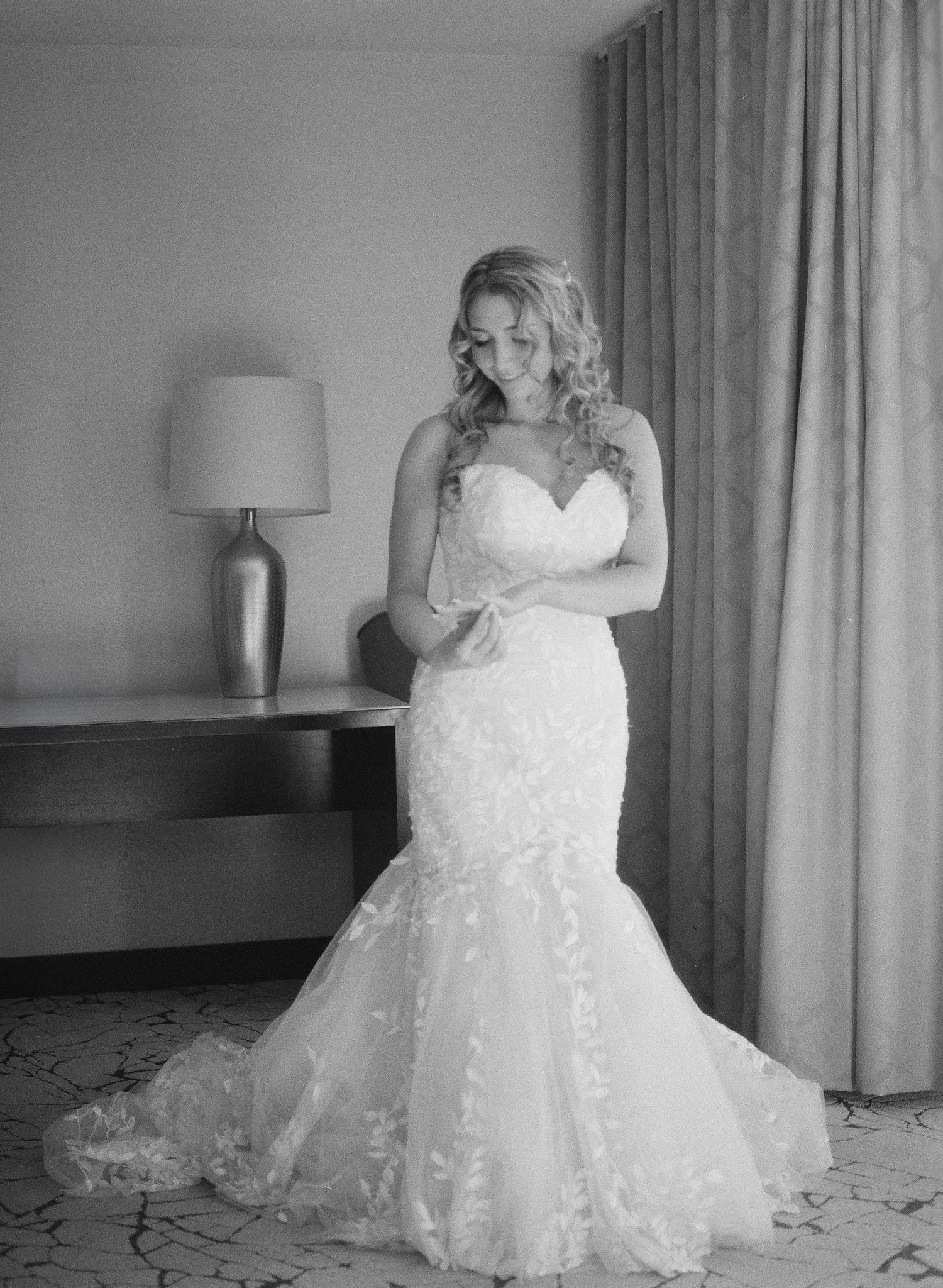 A sweeping view of a white lace wedding gown with intricate details shown from multiple angles in a hotel room setting.