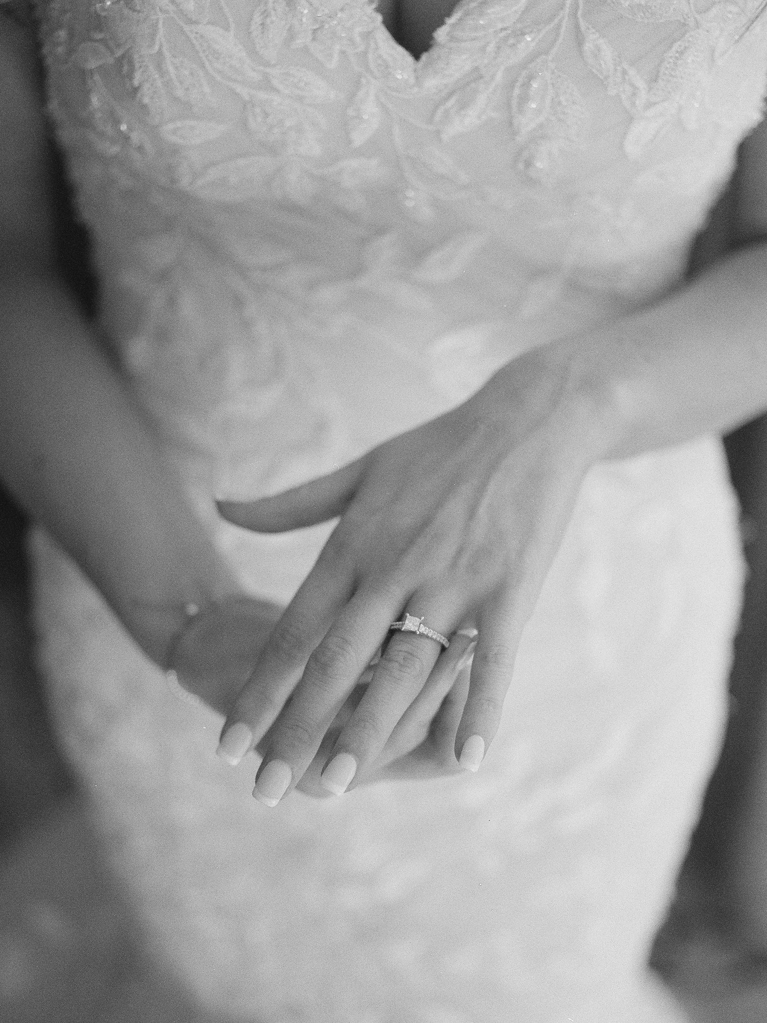 A close-up black and white photo sequence showing a delicate engagement ring on a woman's finger against a white dress.