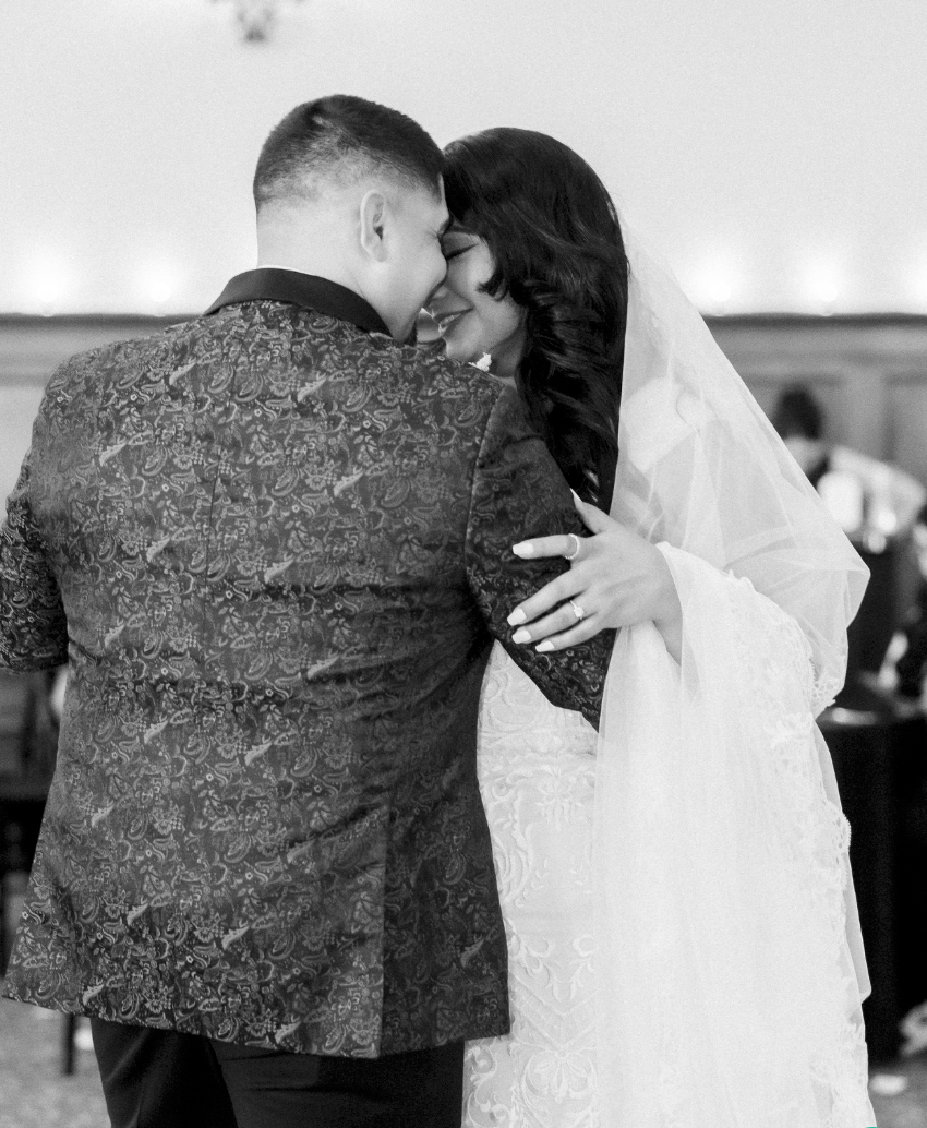 A couple in wedding attire share an intimate kiss with the groom holding a textured gray stone in front of them.