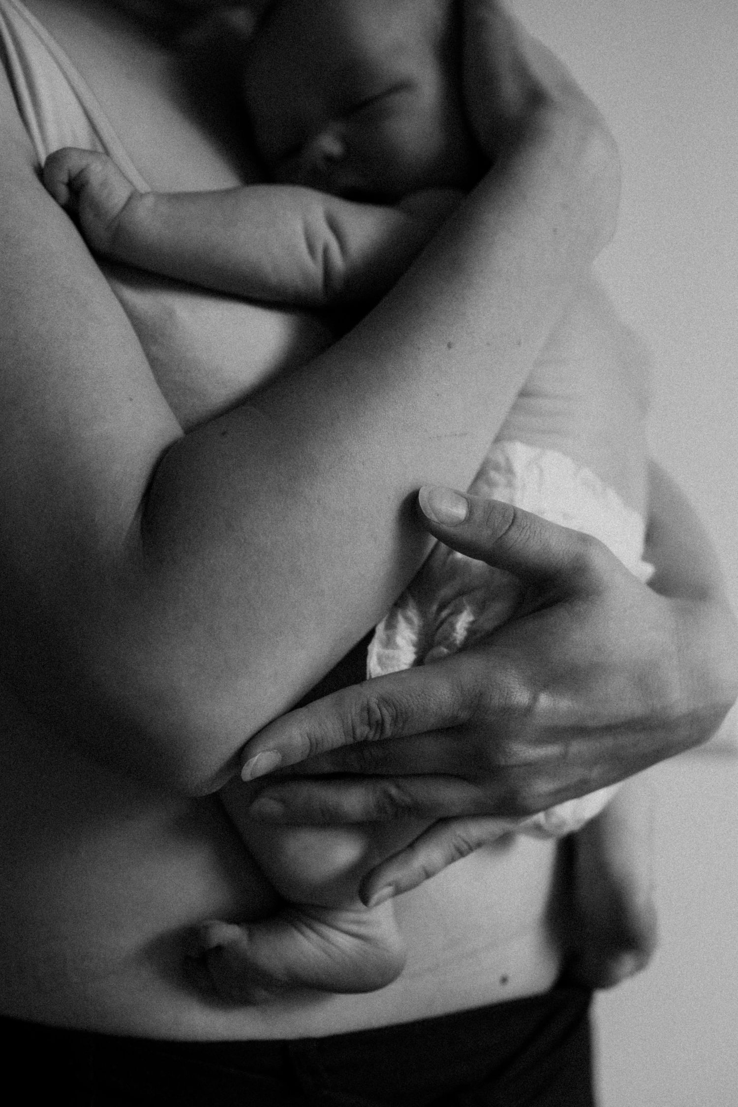Vastasyntynyt vauva äidin rintaa vasten turvallisesti perheen kotona postpartum- ja vauvakuvauksessa. Äidillä rauhoitteleva ilme. Rehellinen