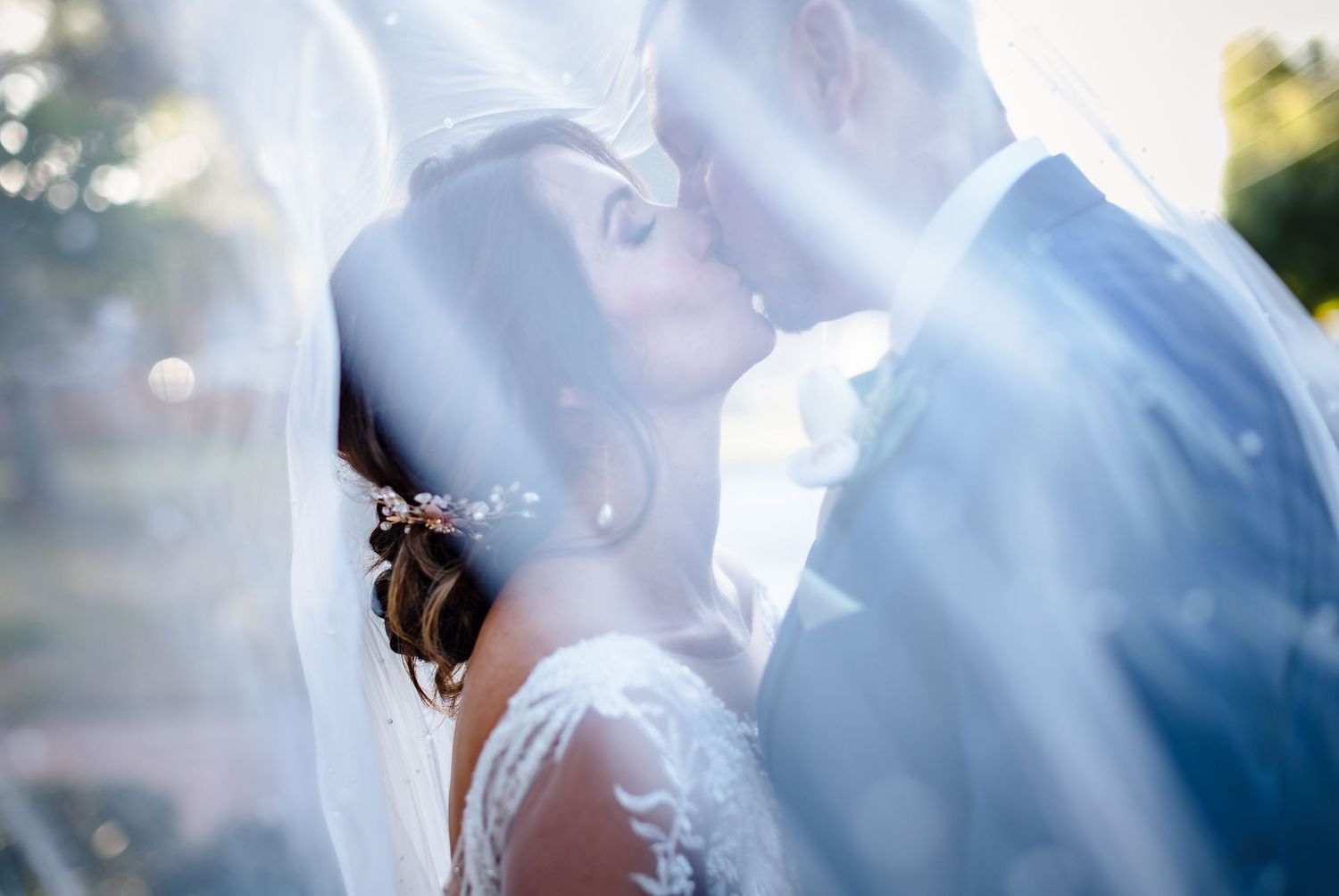 Romantic sunlit wedding kiss captured through delicate veil.