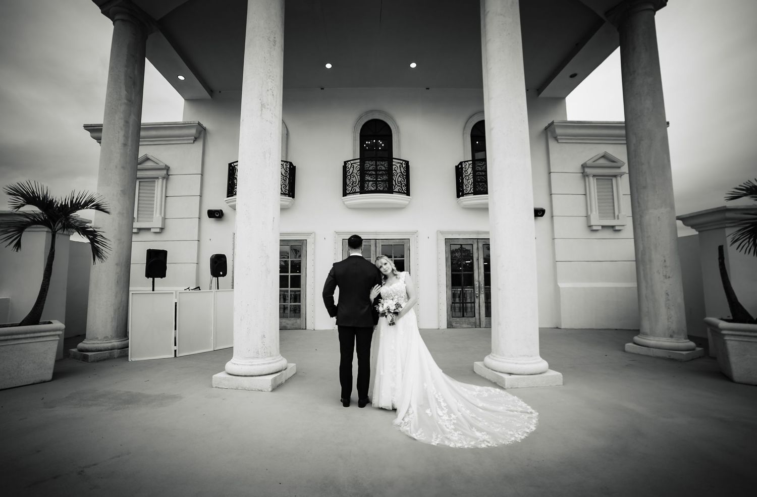 Black and white photo of newlyweds at classic white columned building entrance.
