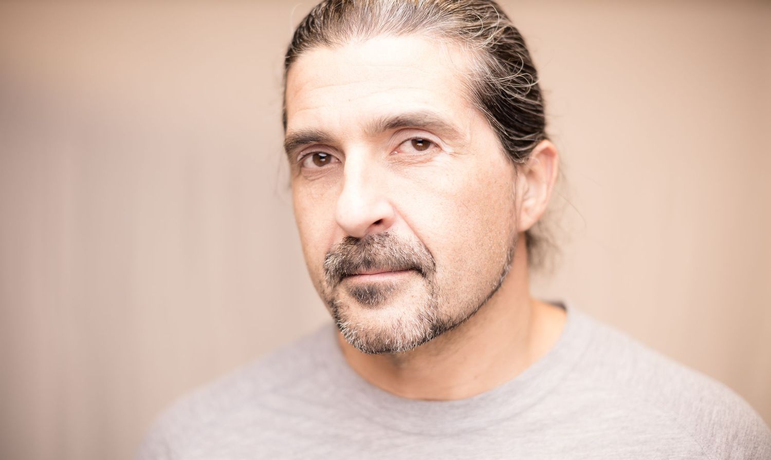 Close-up portrait of man with goatee and long hair against warm background.