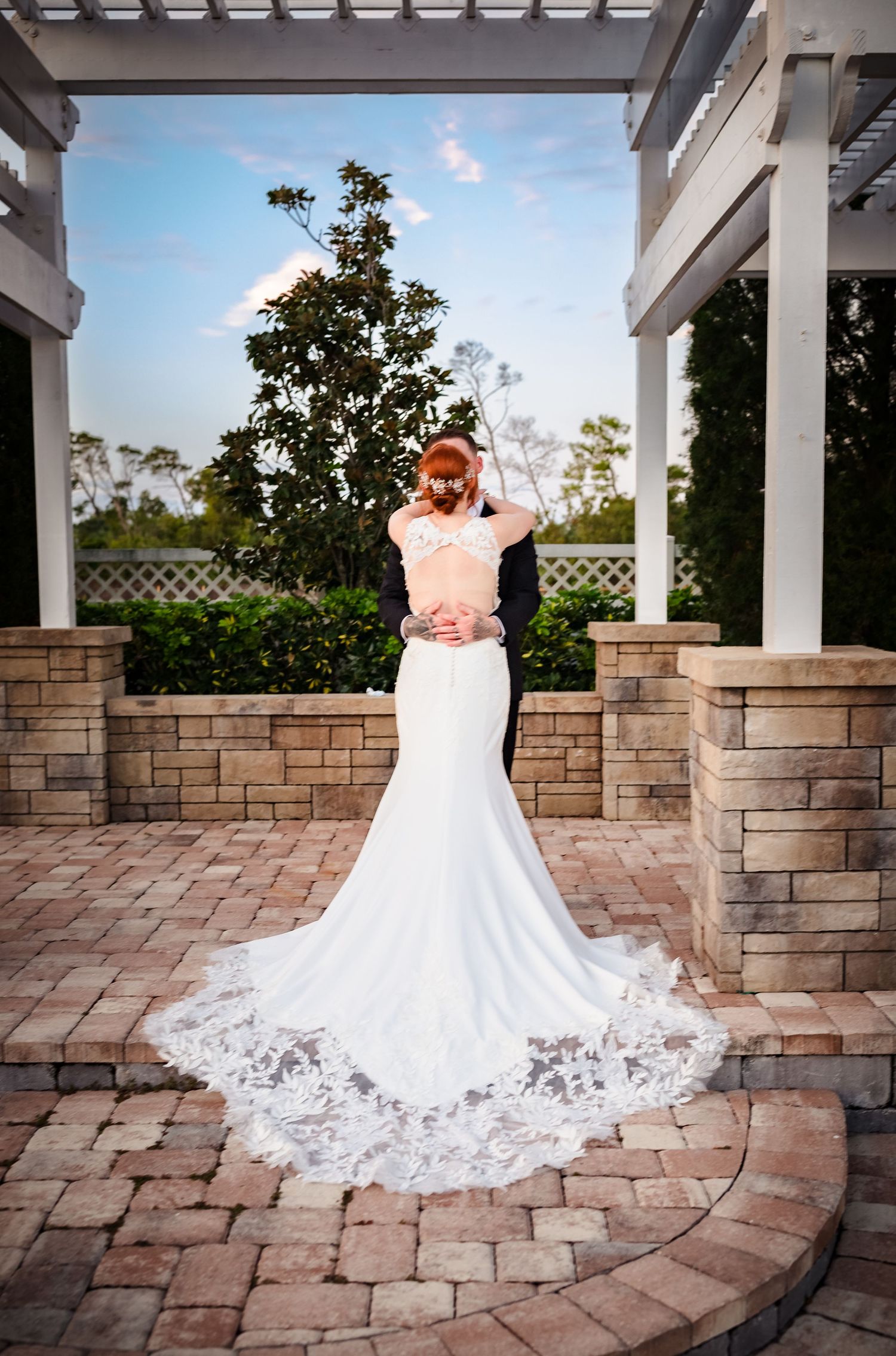 A stunning bridal portrait showcasing a fitted lace wedding gown with cathedral train on brick patio.