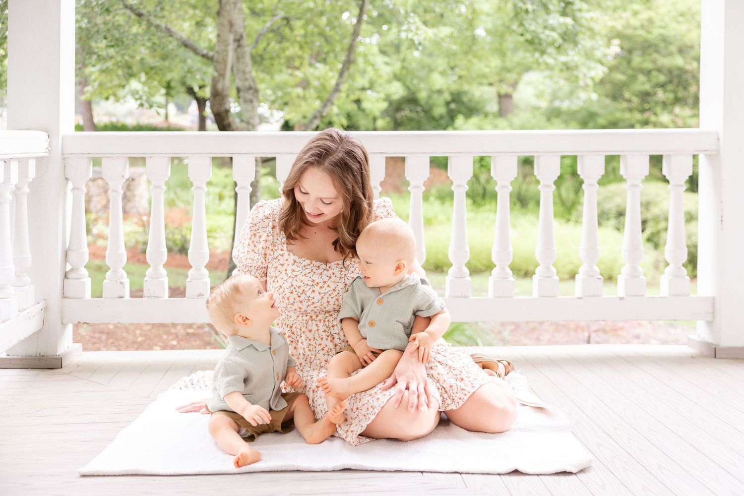 A tender moment captured on a front porch swing as a parent in a floral dress sits and plays with a baby.
