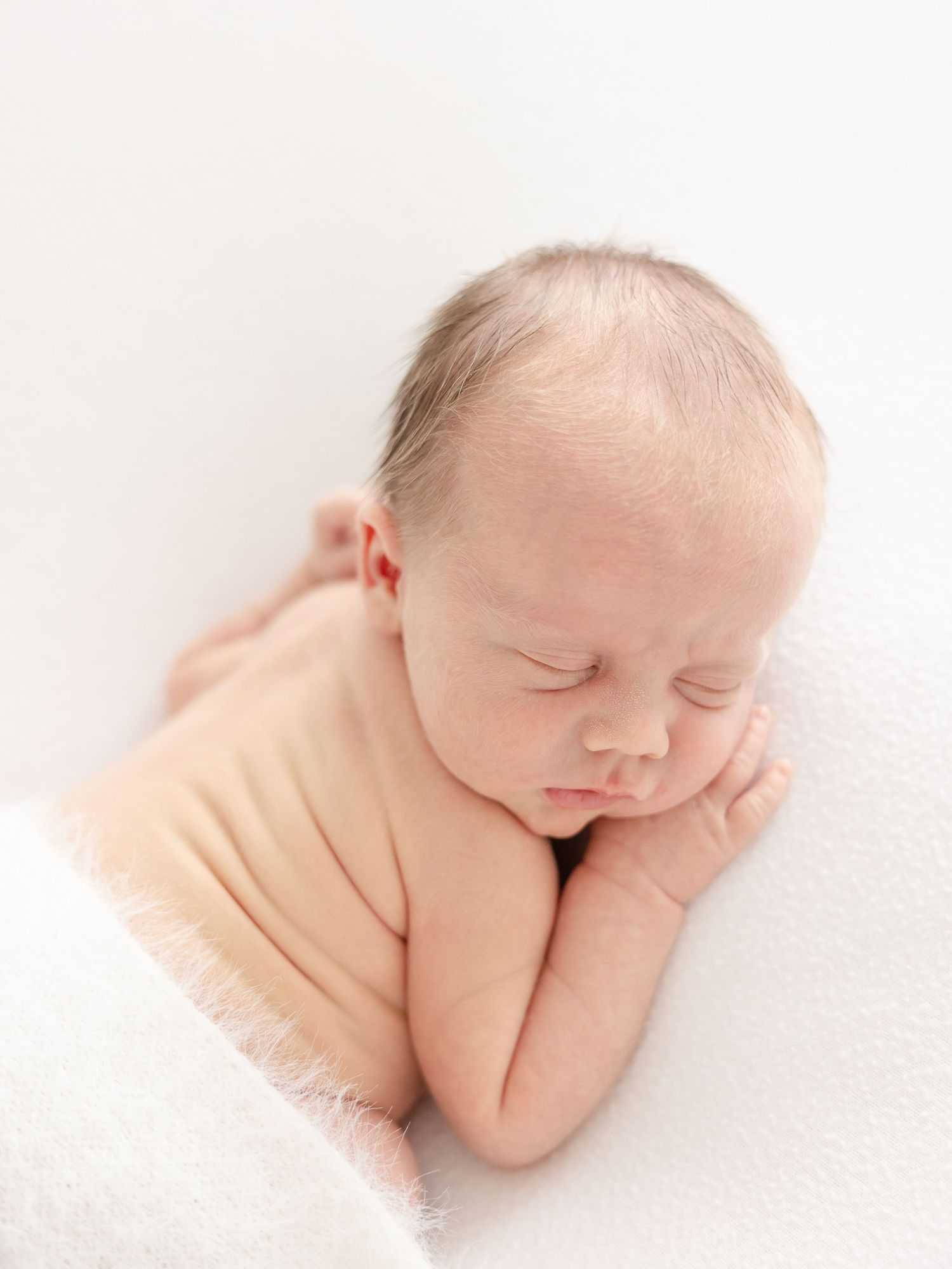 A sleeping newborn baby laying on a white blanket by Columbus, GA baby photographer.