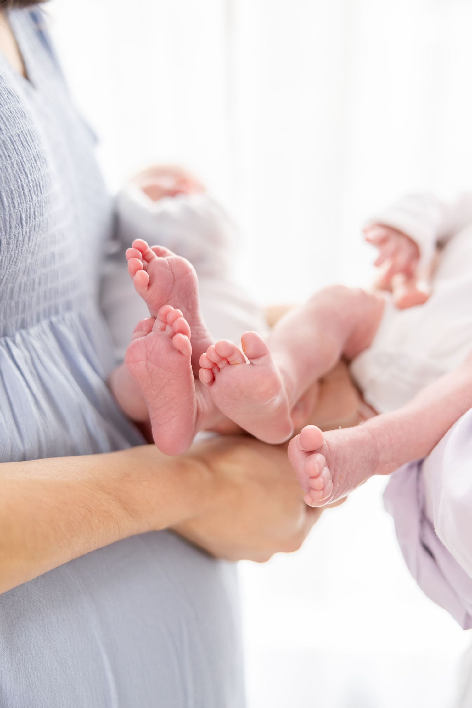Close up of tiny newborn baby feet being gently held in adult hands against soft light background at their Columbus, GA newborn session.