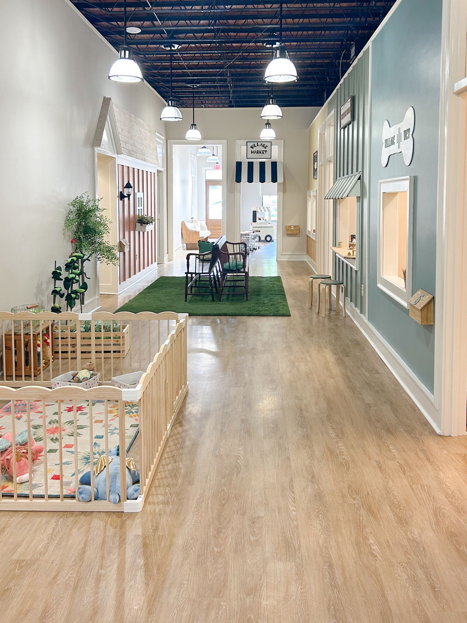 Modern daycare interior with artificial turf play area, wood floors, and bright lighting in a long hallway design.