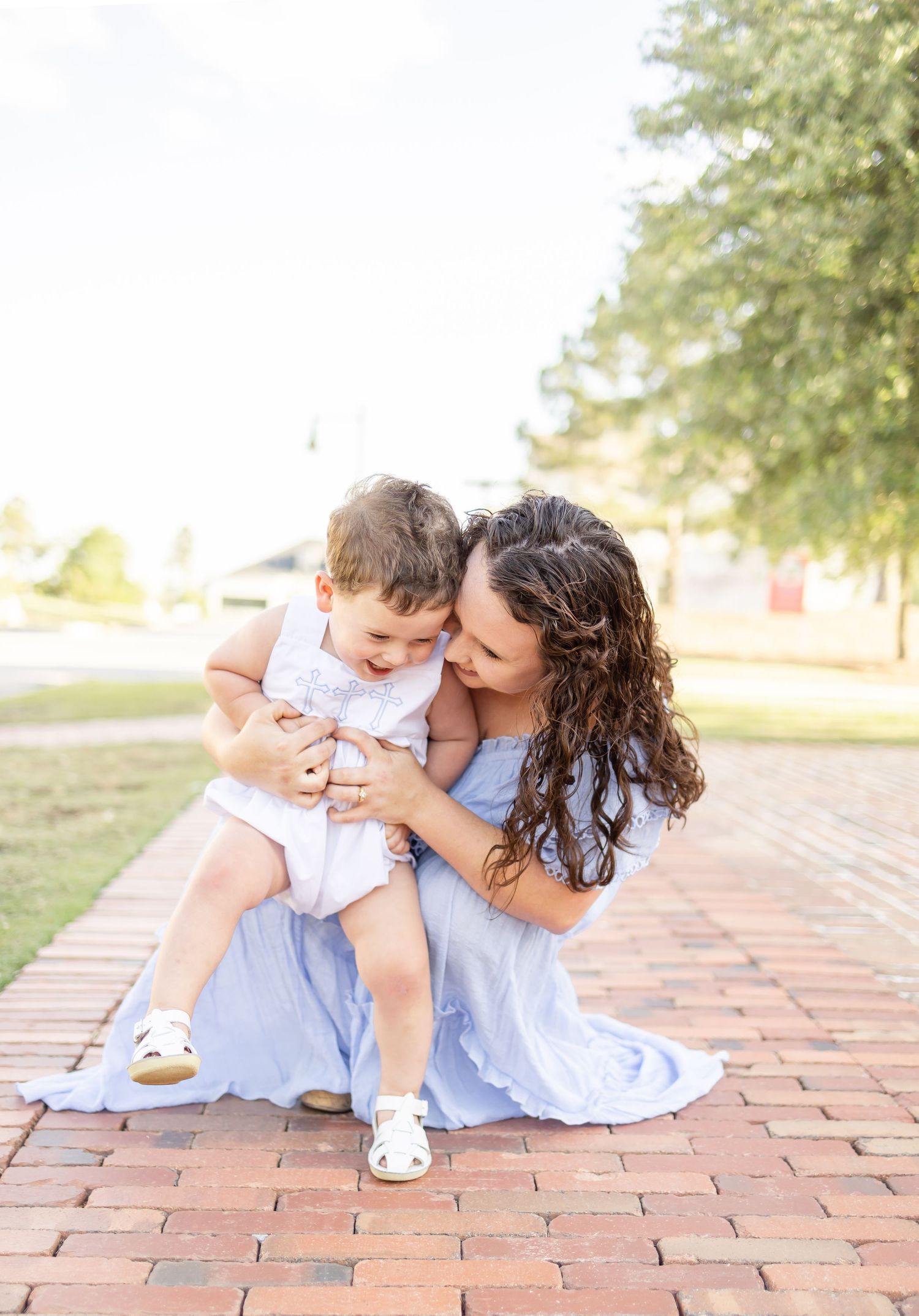 A mother in a blue dress hugs her toddler on a brick path outdoors during their spring family portraits in Columbus, GA.