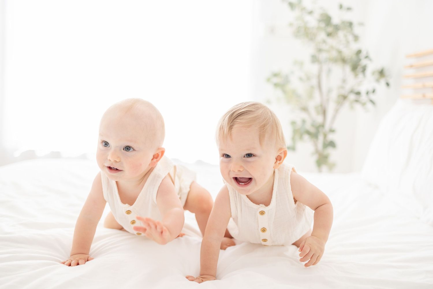 Twin baby boys crawling and smiling on a white bed at their one year milestone session by Columbus, GA baby photographer.