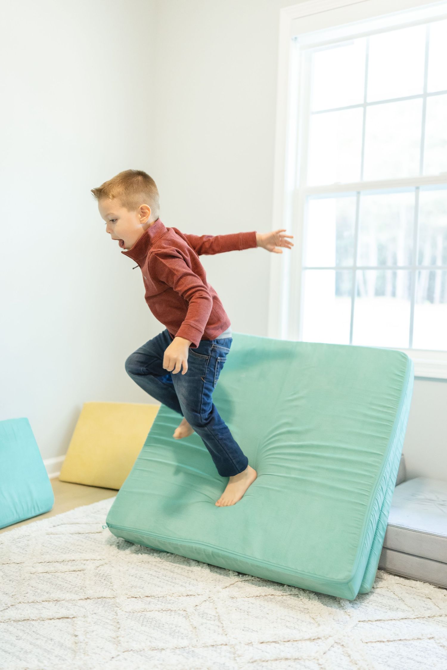 Young boy jumps from his green nugget cushion to another during his lifestyle family portrait session in Columbus, GA.
