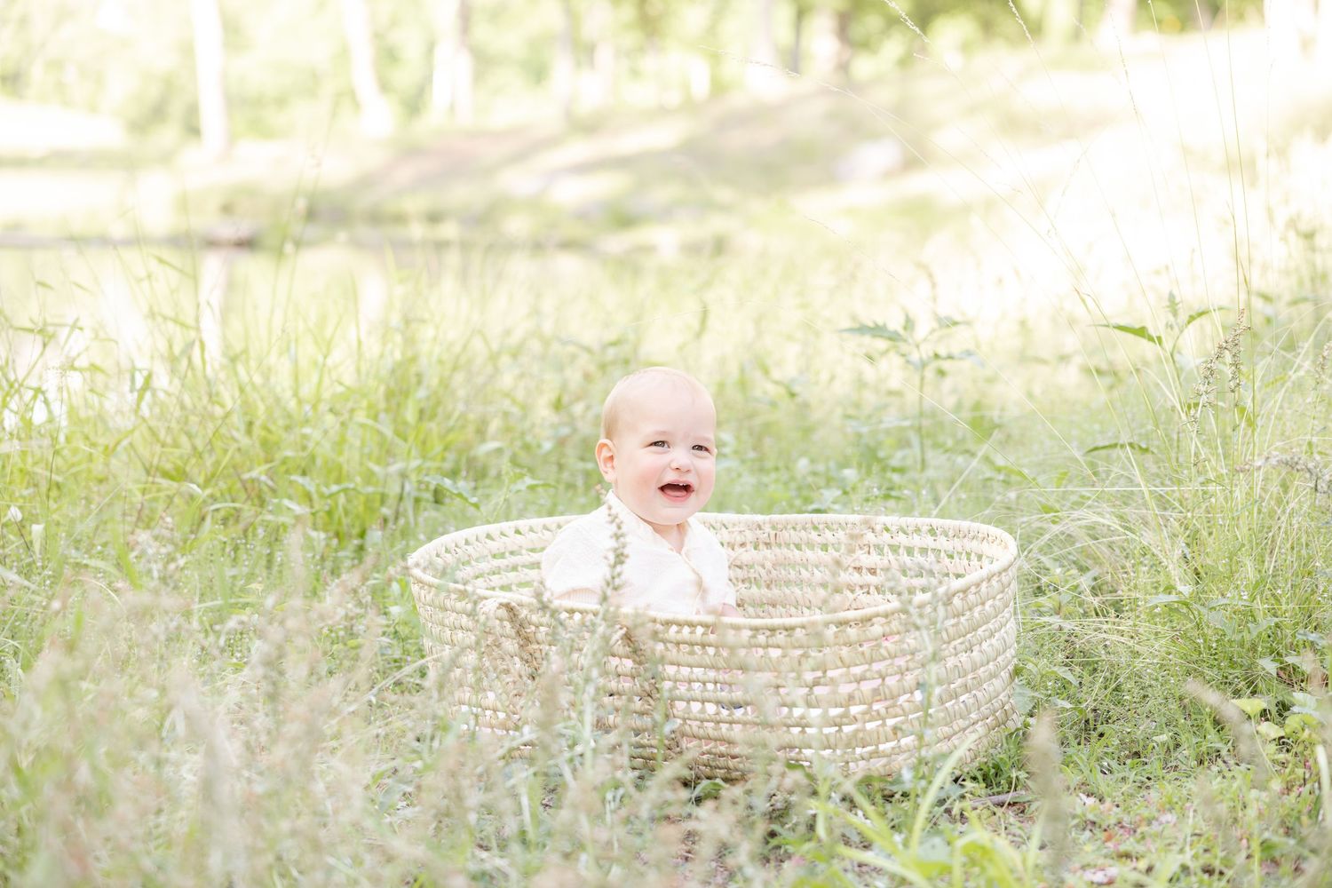 A happy baby sitting in a woven basket outdoors surrounded by lush green grass in the spring by Columbus, GA family photographer.