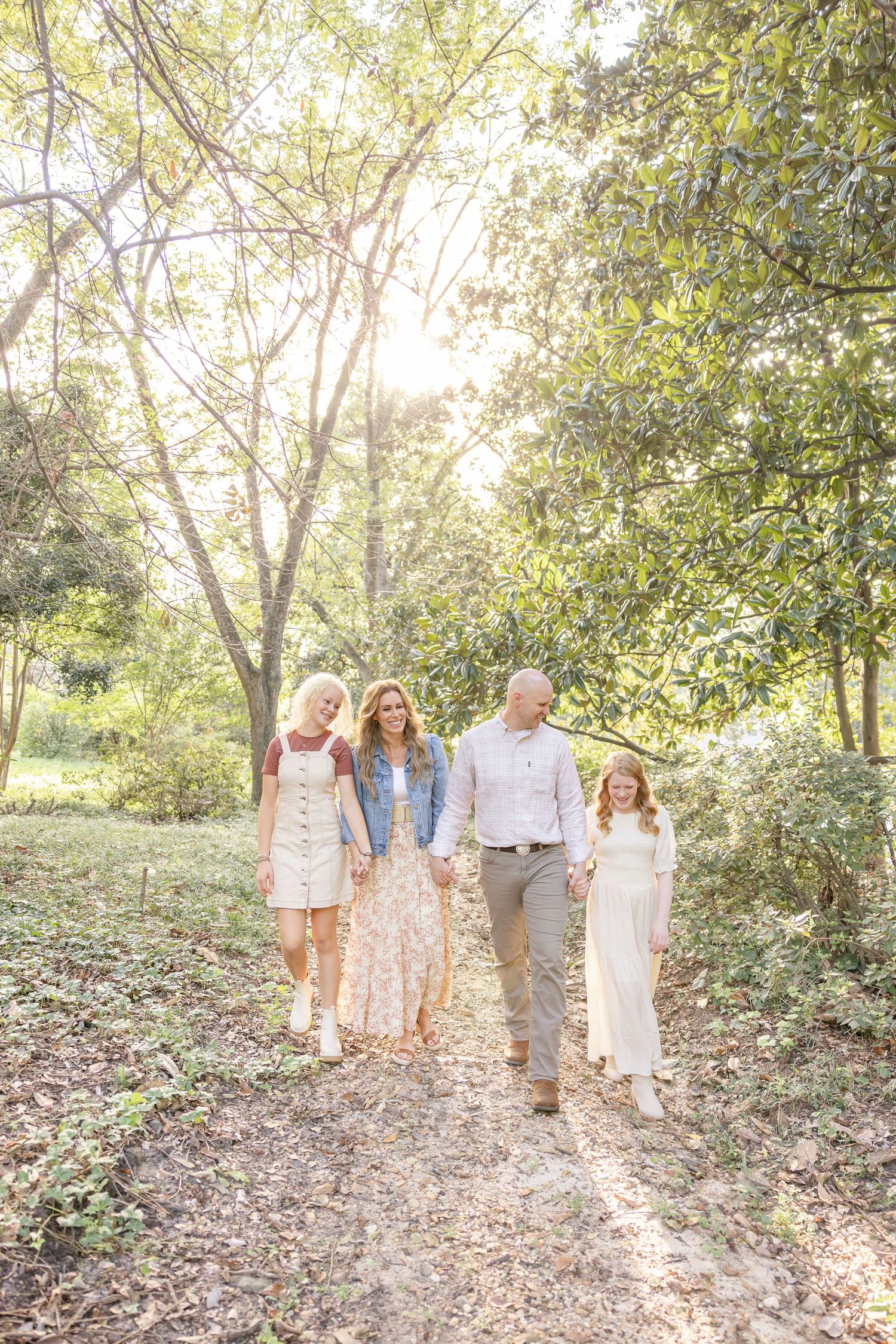 A family walks together on a sunlit wooded path through trees on a bright autumn afternoon.