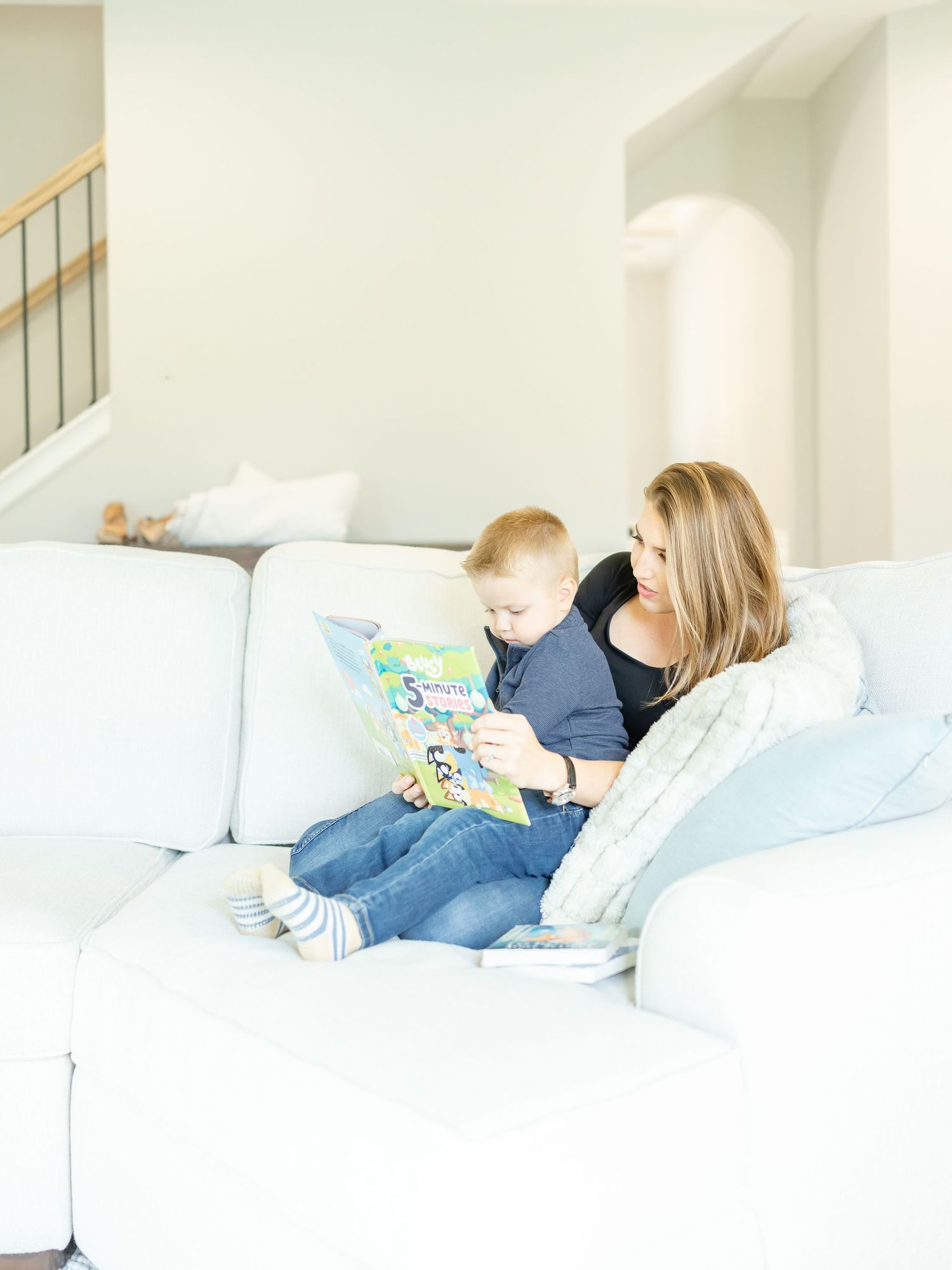 A mom sits on the couch reading to her son at their in-home lifestyle family portrait session in Columbus, GA.