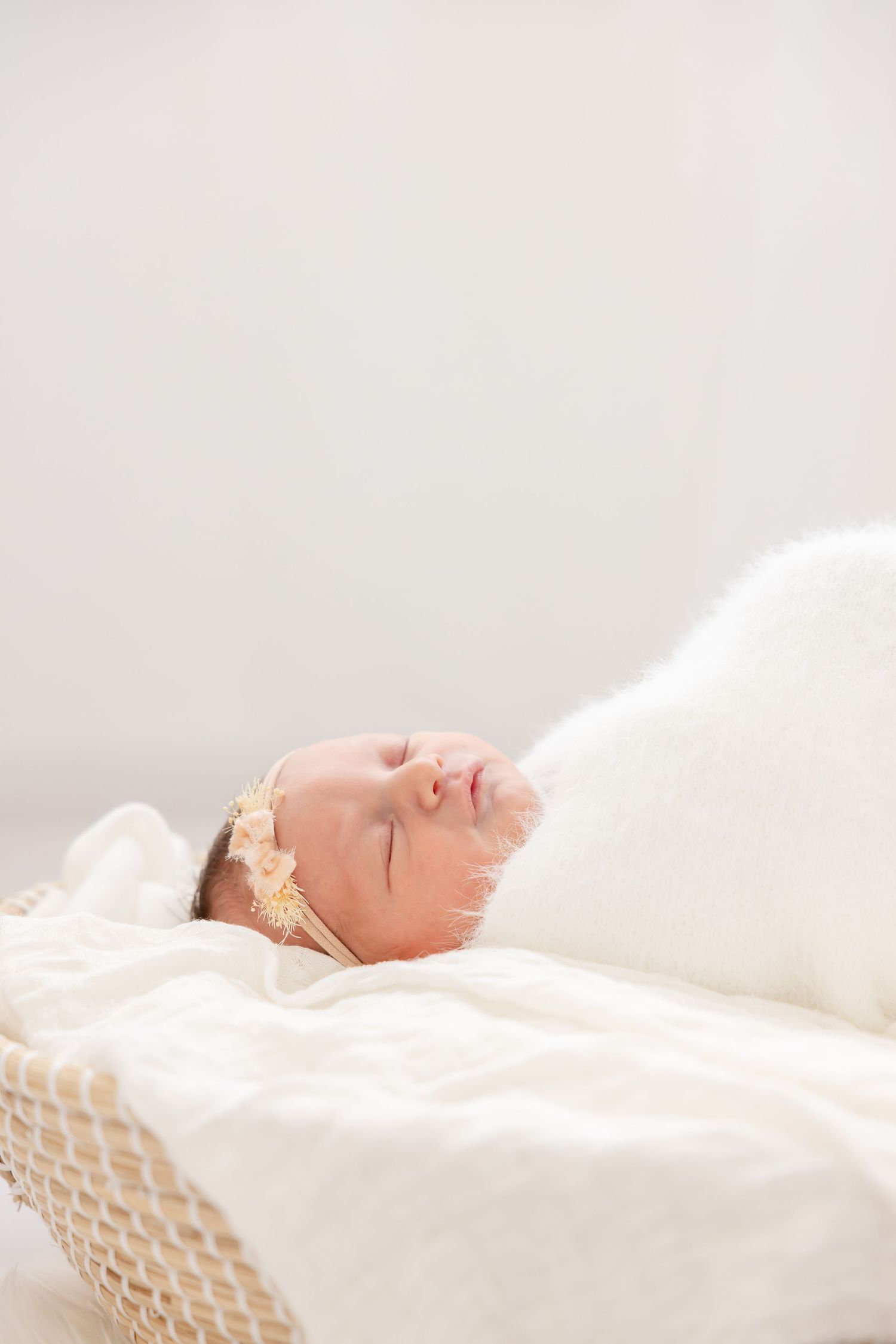 A sleeping newborn baby swaddled in white fabric lies peacefully on a soft textured surface.