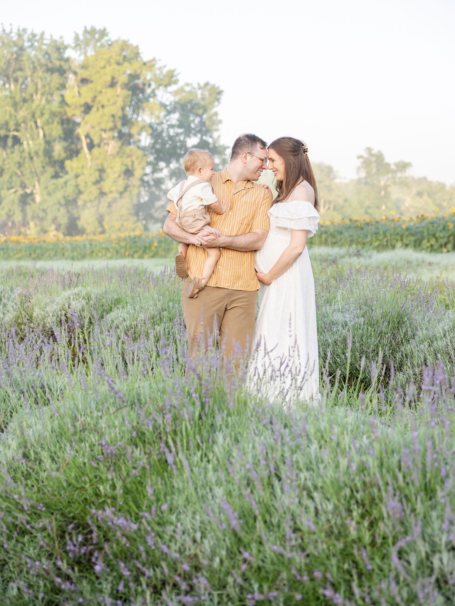 A couple embraces tenderly in a sunlit lavender field during a romantic outdoor photoshoot.