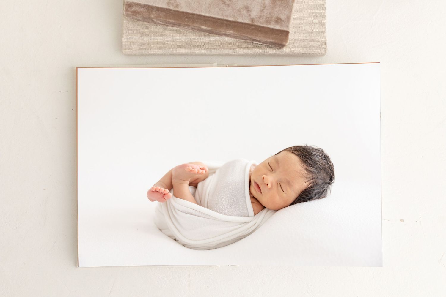 Peaceful newborn baby swaddled in white wrap, sleeping soundly on a soft white surface in a serene studio setting.