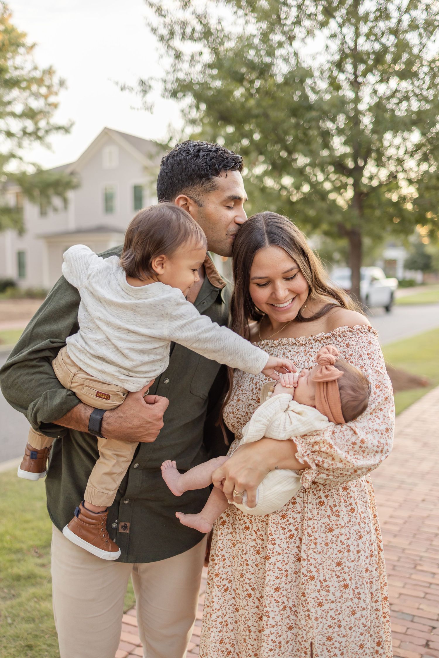 A happy family shares a tender moment together on a brick sidewalk during golden hour at their Columbus, GA photography session.