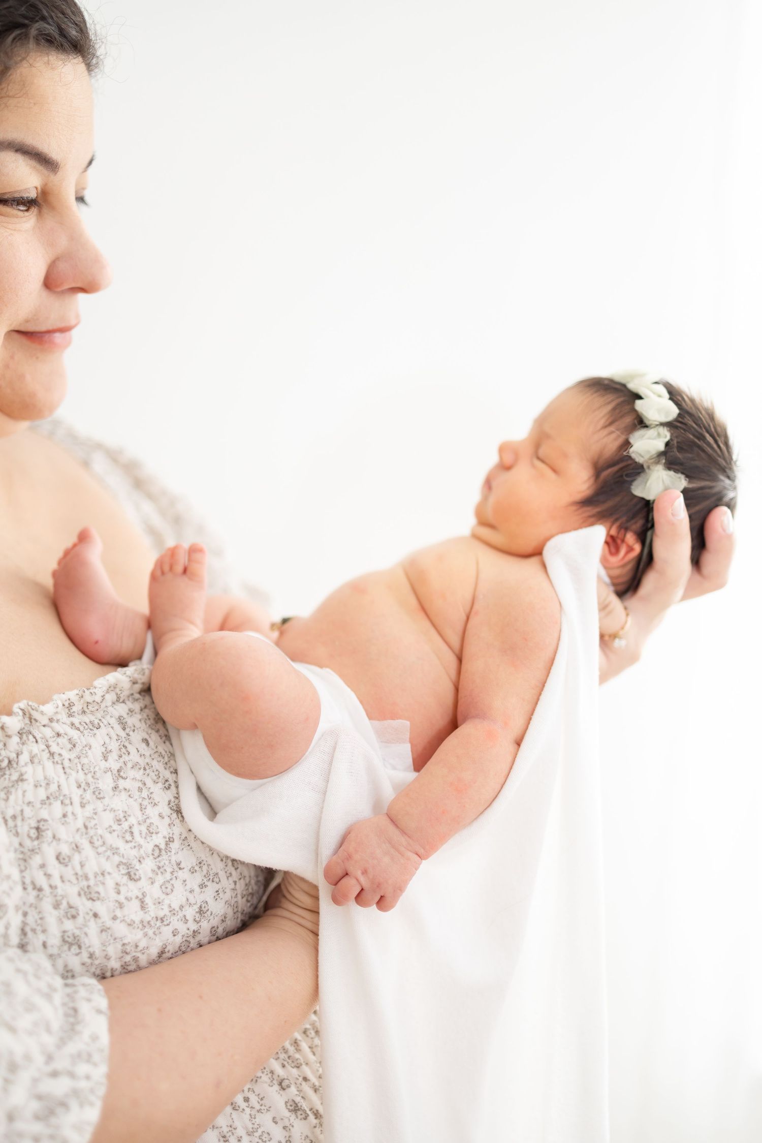 A tender moment between mother and her newborn wearing a delicate white headband at newborn photoshoot in Columbus, GA.