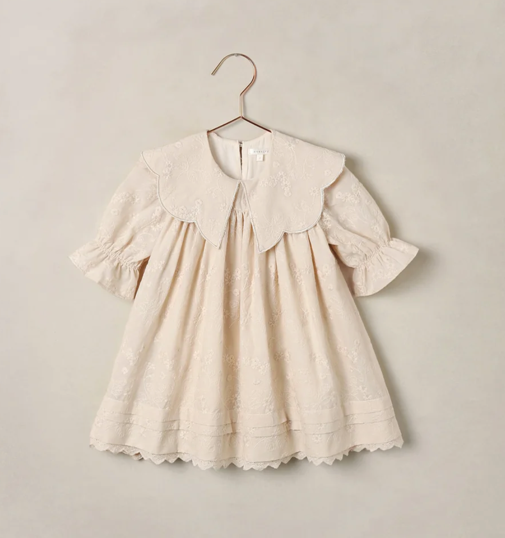 Cream eyelet embroidered baby girl dress with scalloped hem, ruffled sleeves, and oversized Peter Pan collar on hanger.