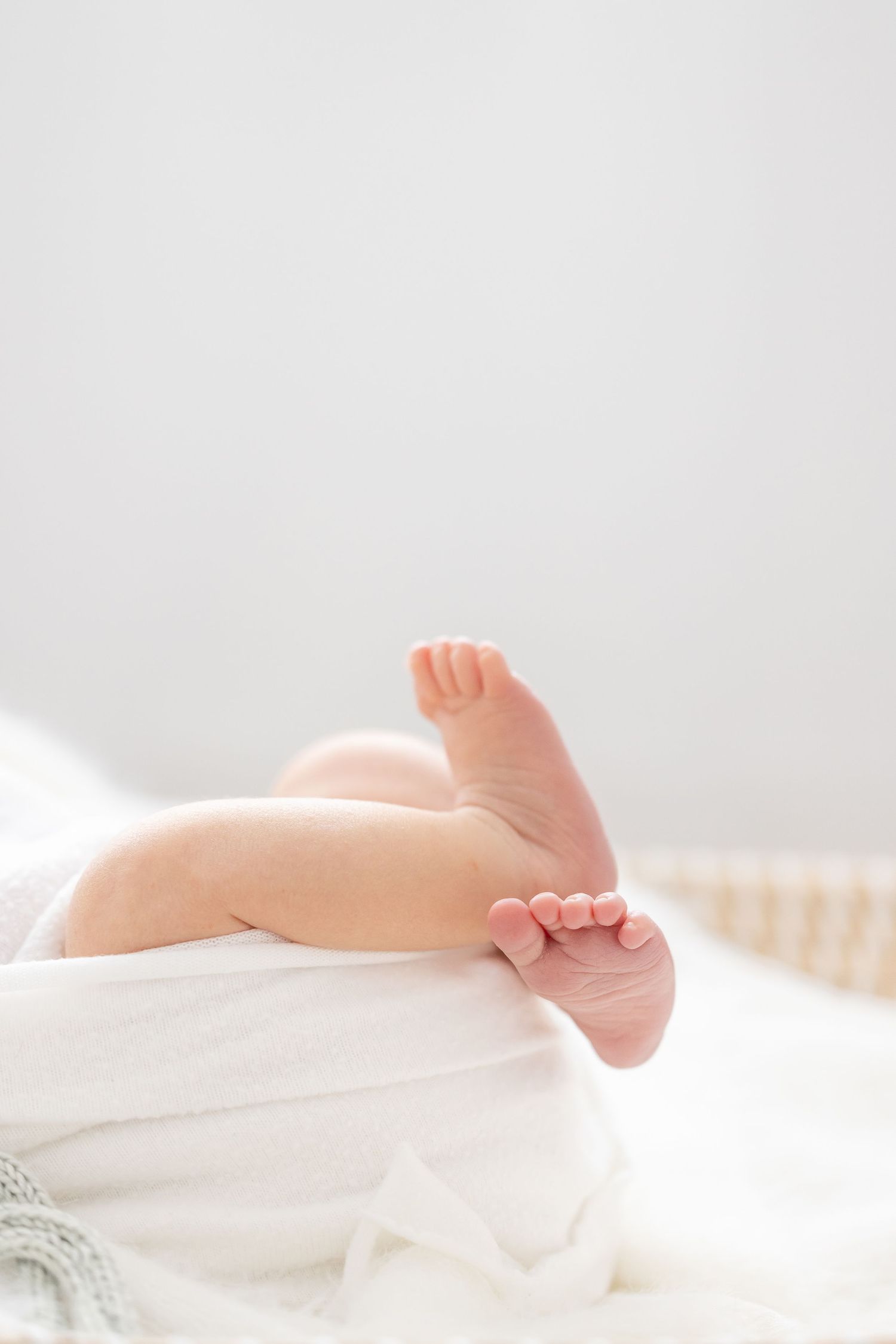 Close up of tiny baby feet under white cozy blanket in soft morning light at newborn photoshoot in Columbus, GA.