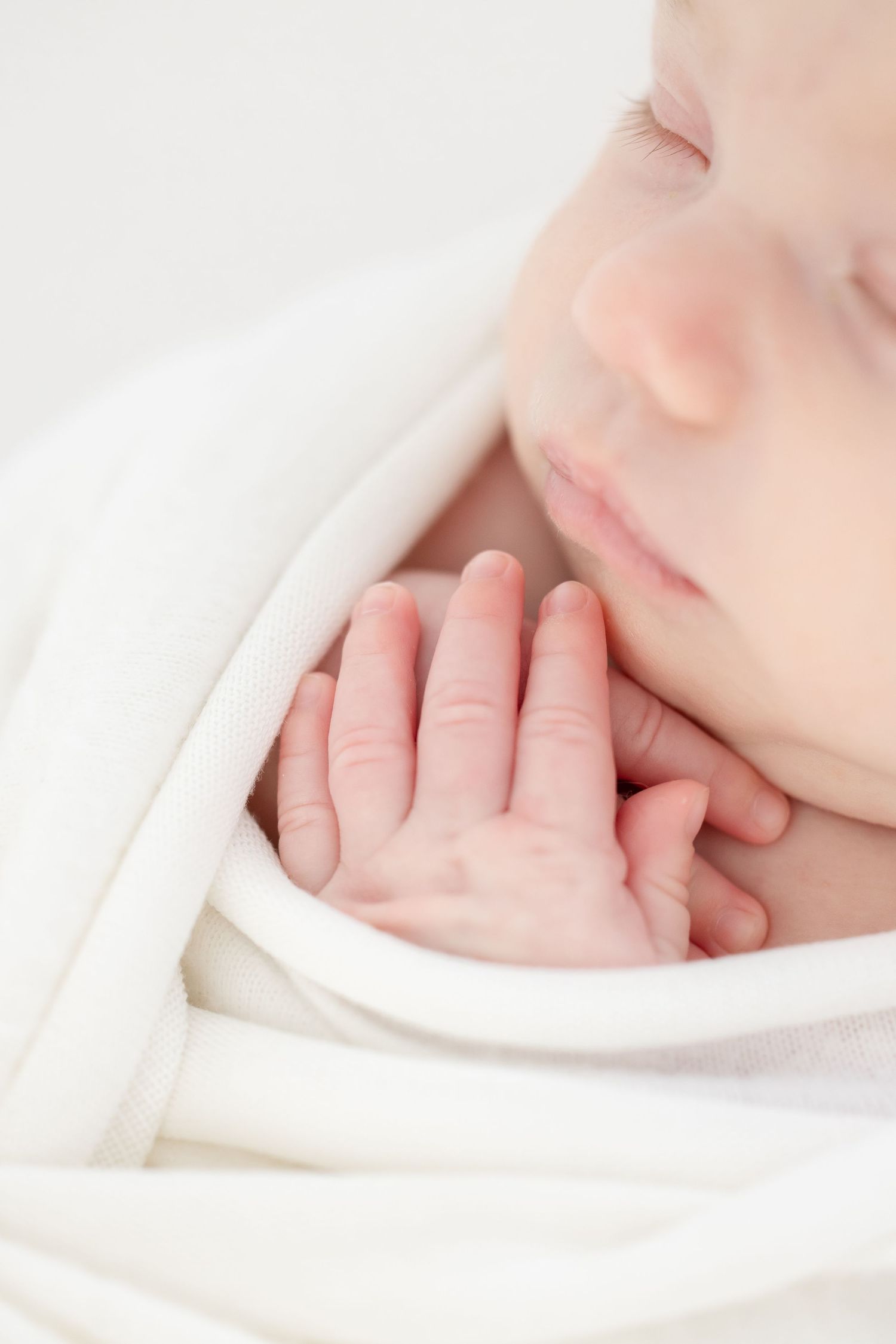 A sleeping baby's tiny hand rests gently against soft white blankets in a peaceful close-up shot by Columbus, GA newborn photographer.