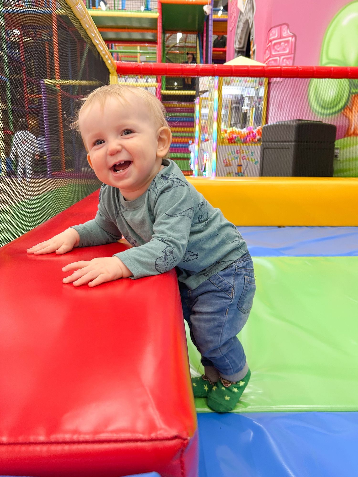 A toddler in denim and grey clothing plays on colorful padded equipment at an indoor playground in Columbus, GA.