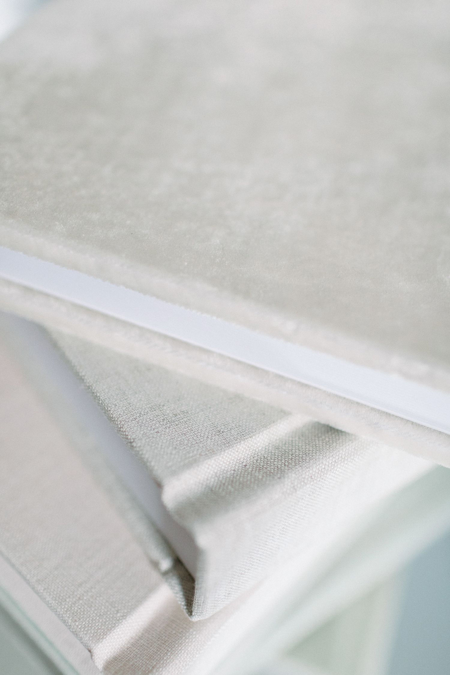 Close-up of elegant white linen photo albums with satin ribbon detail on soft blue background.