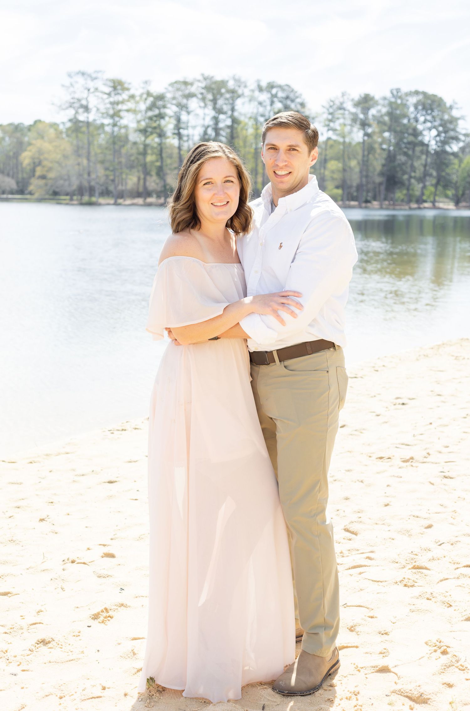 A couple in light colored attire embraces on a sandy beach during their family portrait session in Columbus, GA.