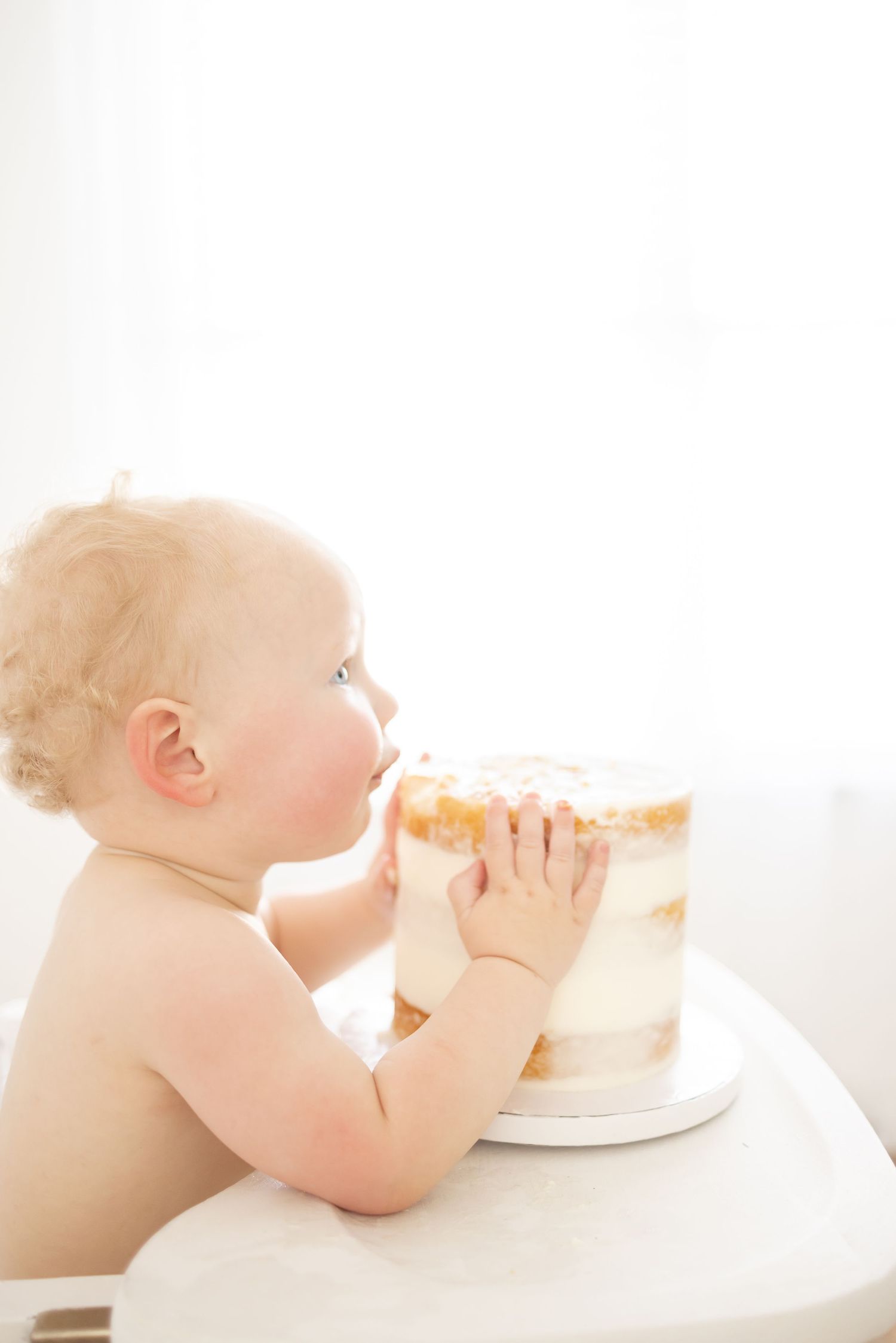 Baby eating a white frosted cake while sitting in high chair at his first birthday milestone session by a Columbus GA photographer.
