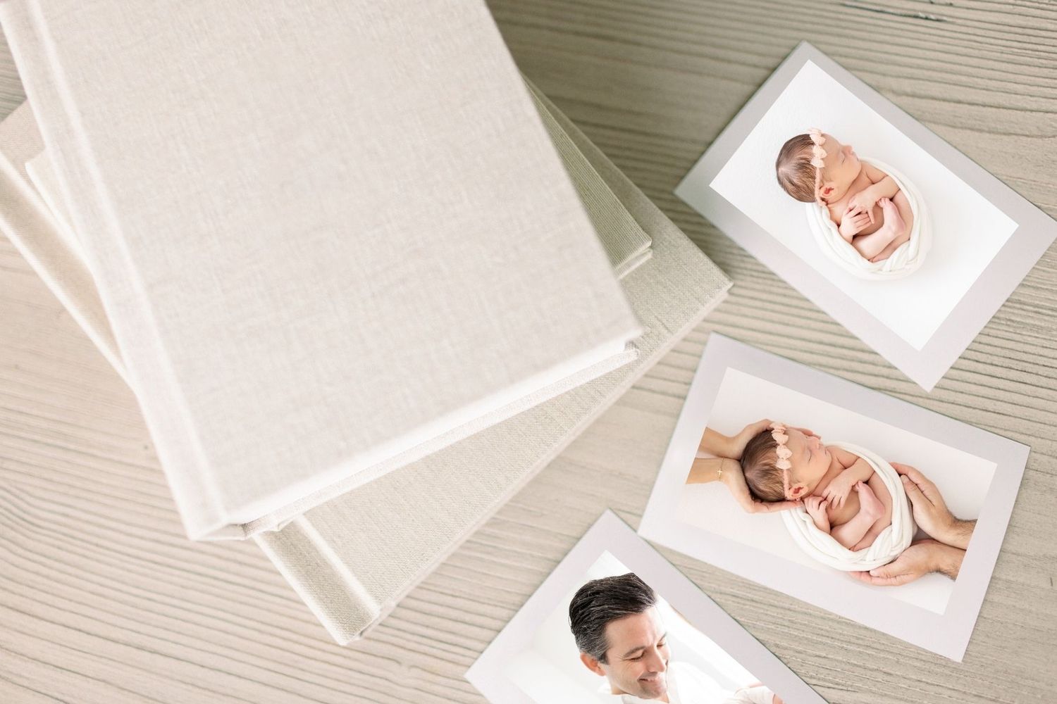 Photo albums with linen covers beside printed portrait photos of a smiling man on a wooden surface.