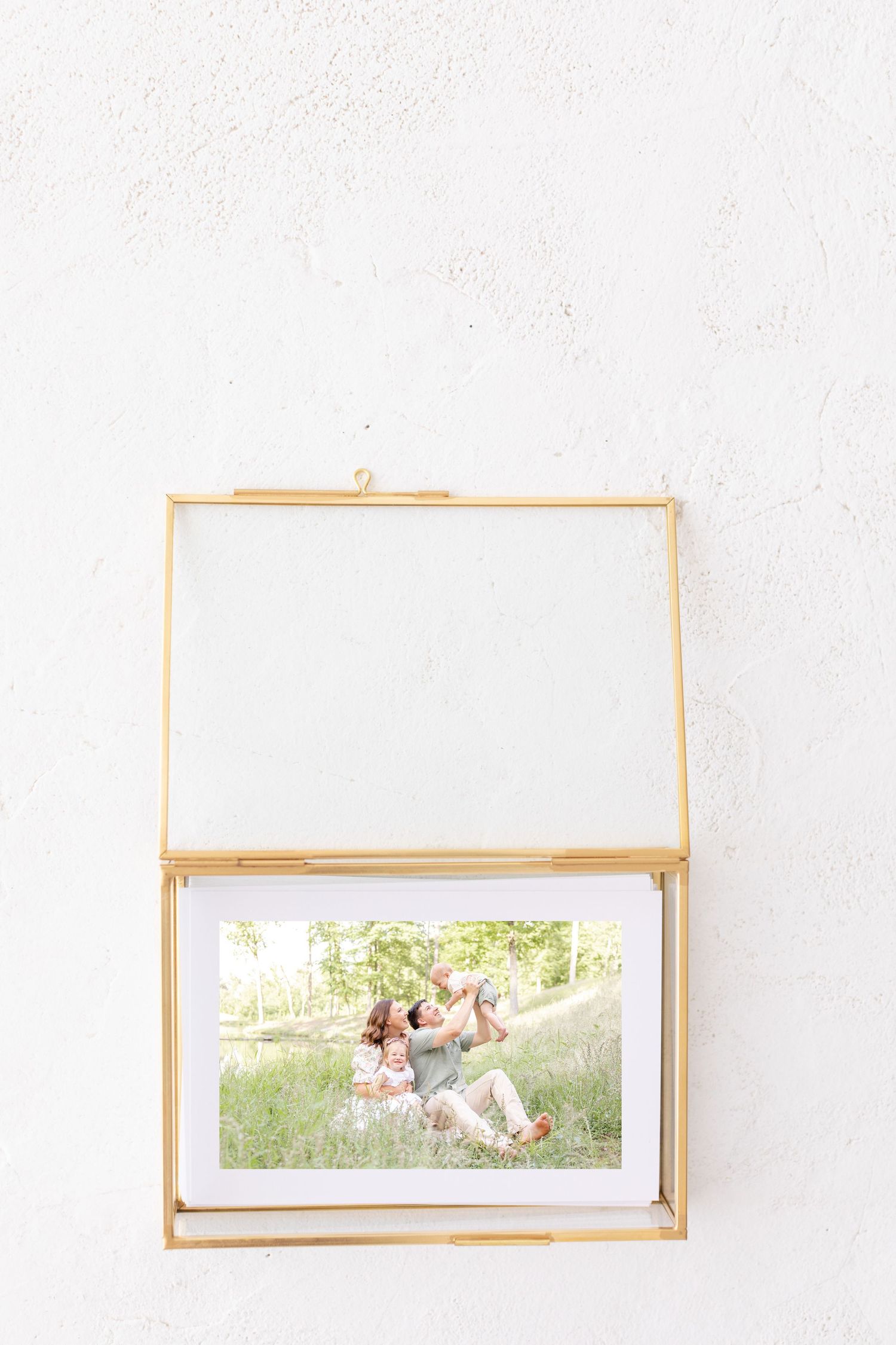 Glass and brass photo display box opened to reveal a portrait photograph placed inside on white surface.