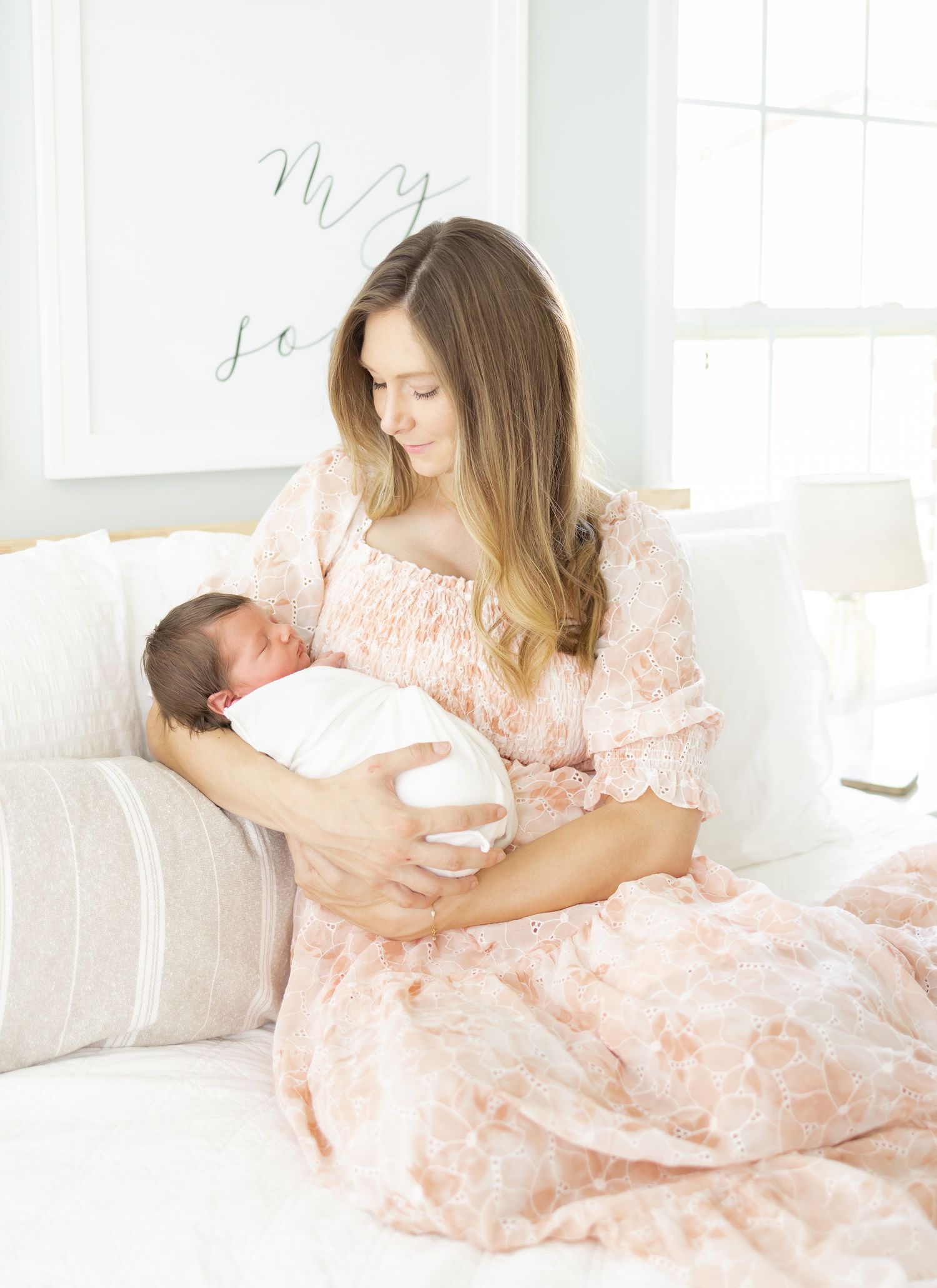 A mother in a pink rests on a white bed while holding and bonding with her newborn baby at her in-home newborn session in Columbus, GA.