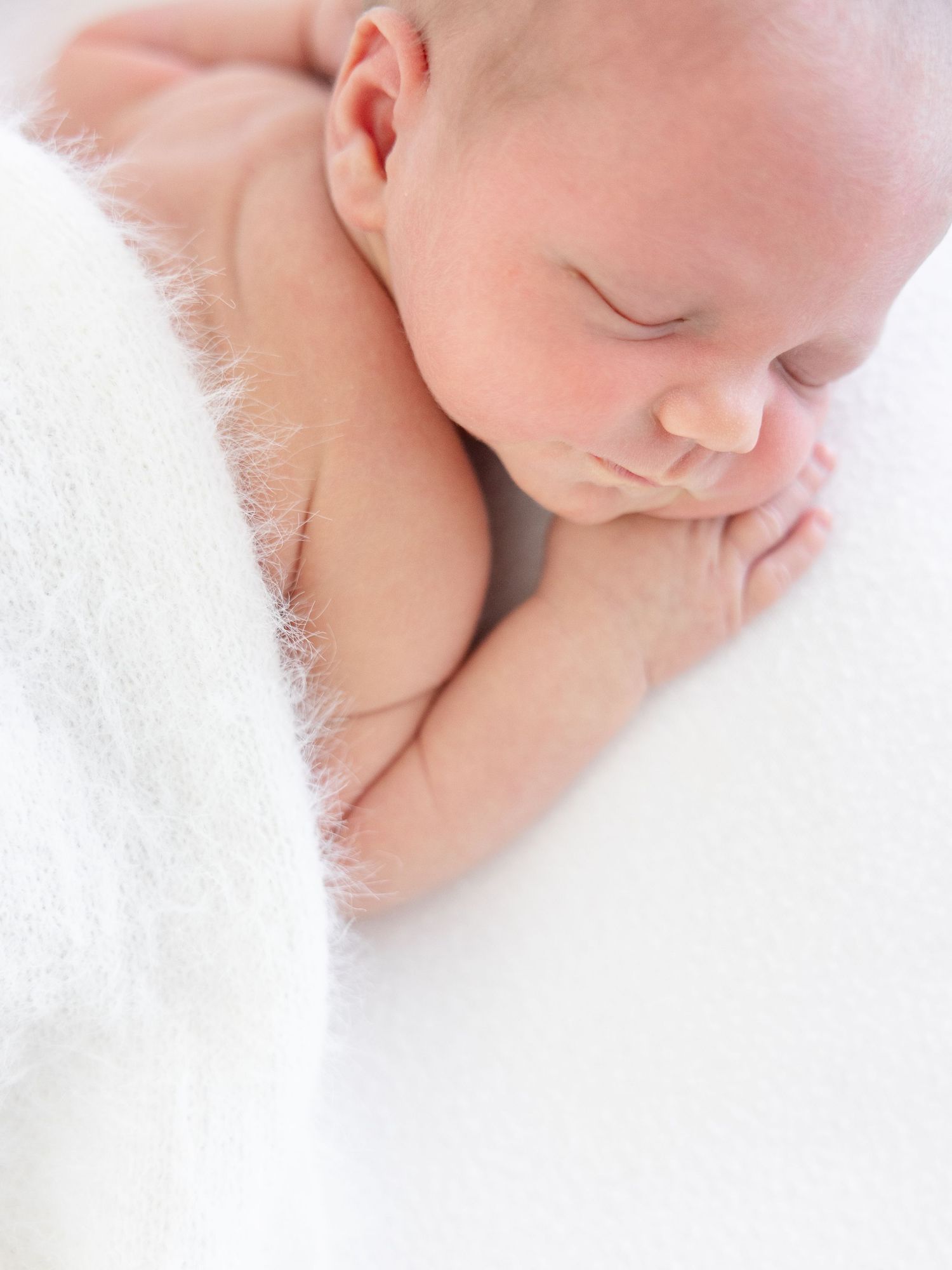Peaceful newborn baby sleeping curled up on a soft white fluffy blanket in a serene portrait.
