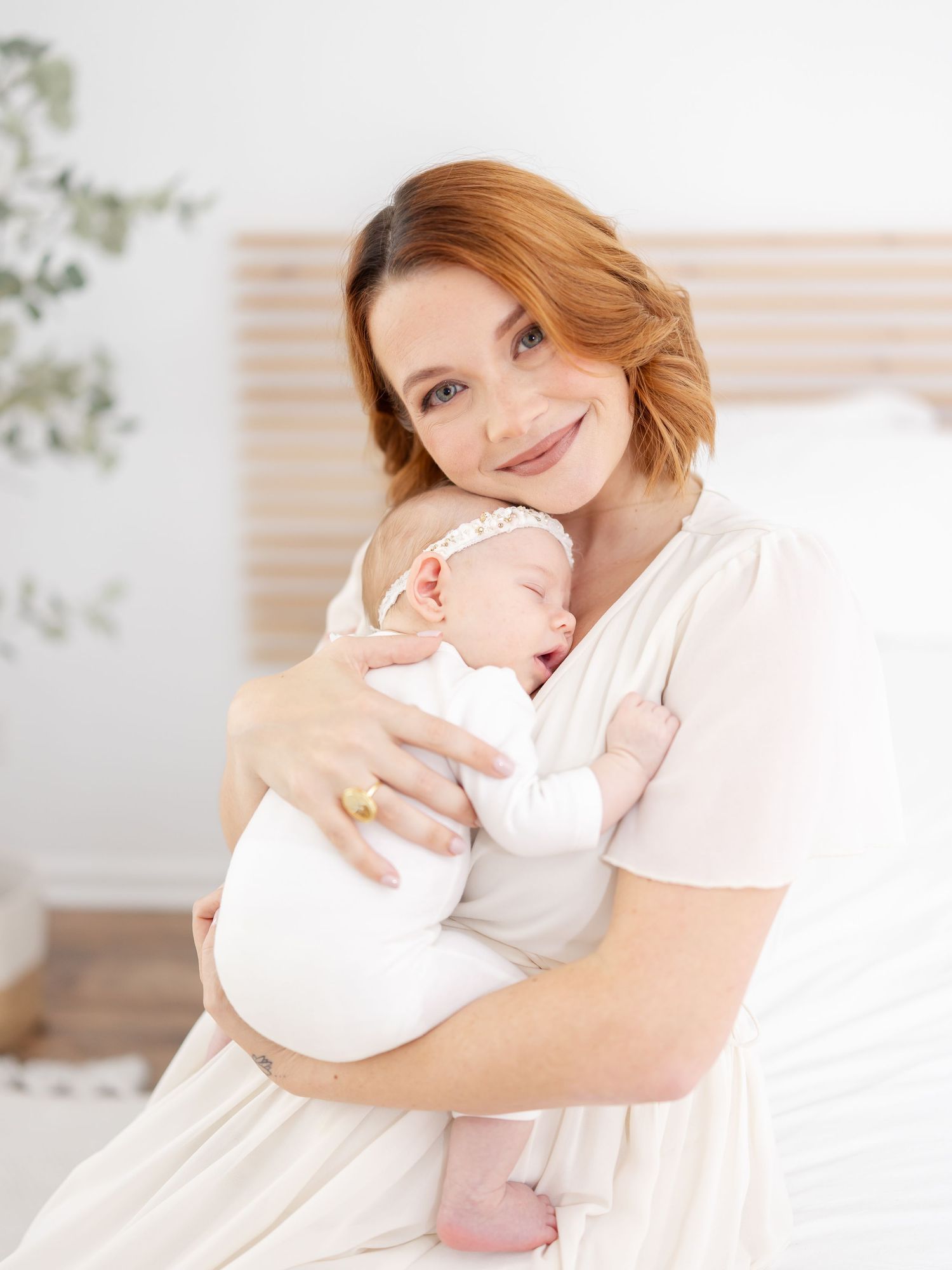 A tender moment as a mother in white dress holds and smiles her sleeping baby against her chest during their Columbus, GA newborn portraits
