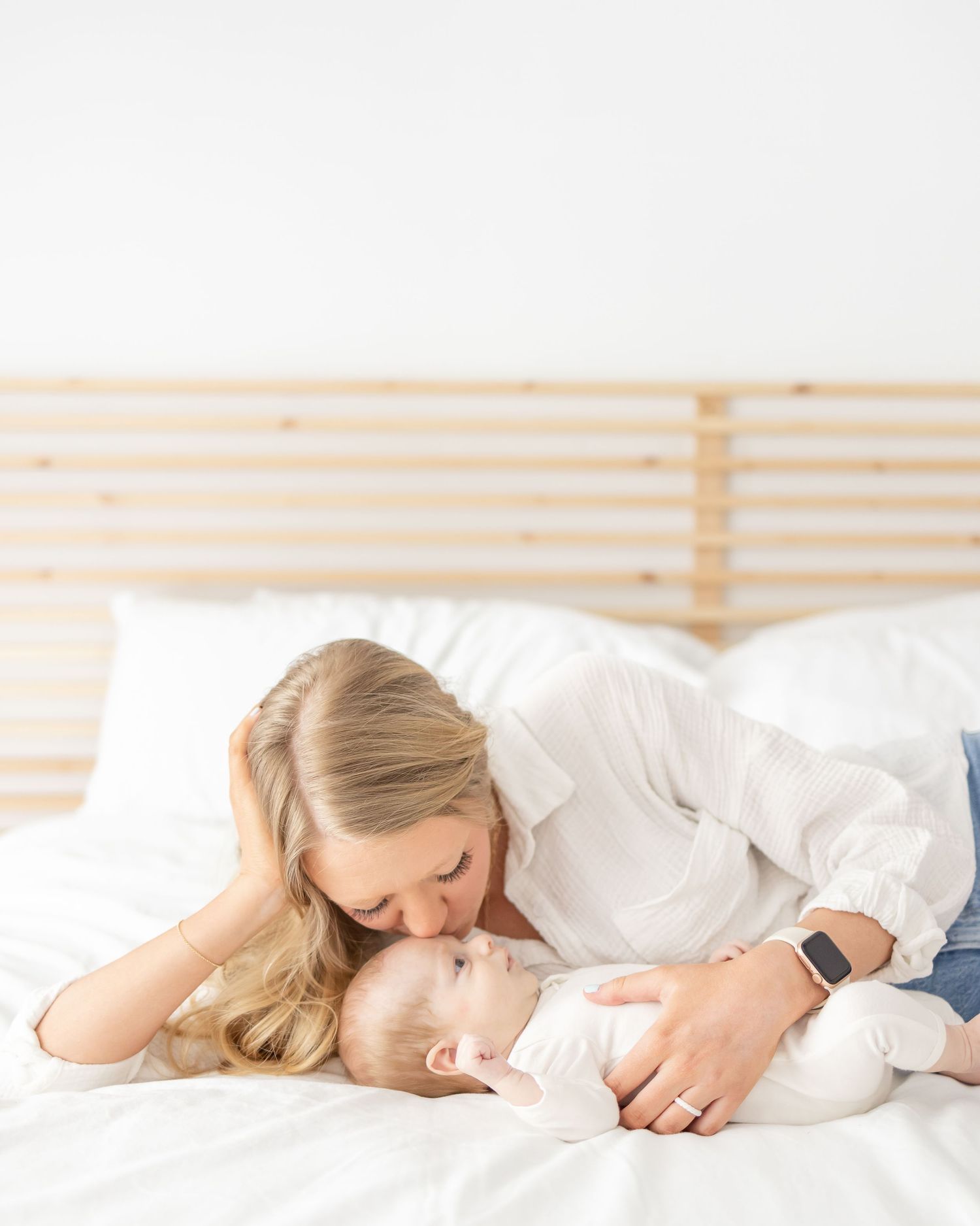 A mother in white clothing lying down on white bedding with her 6 week old baby at their light and airy Columbus, GA newborn portraits.