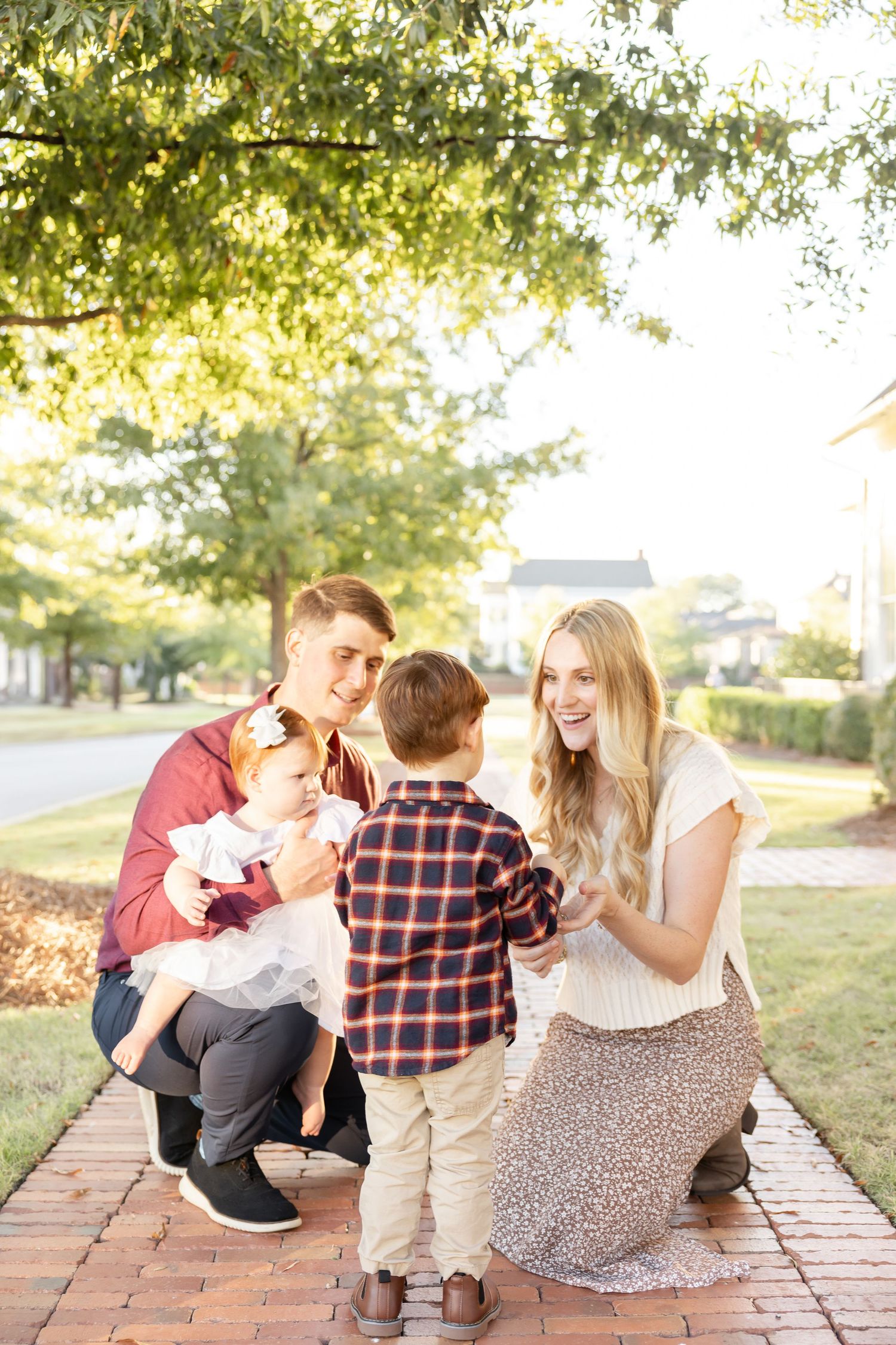 A family shares a tender moment together on a brick pathway while surrounded by sunlit trees on a beautiful autumn day in Columbus, GA.